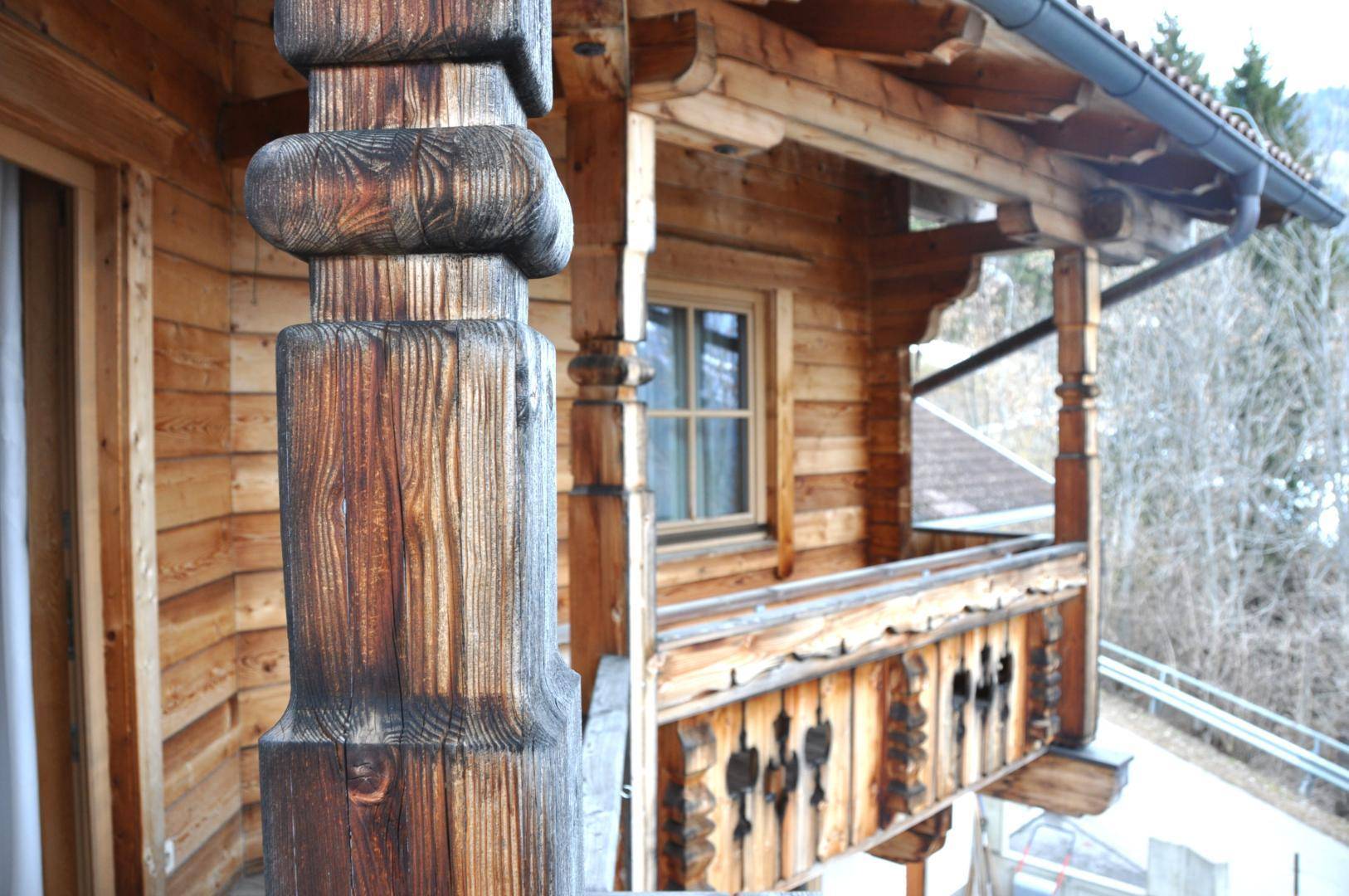 Detailansicht eines kunstvoll geschnitzten Holzgeländers und Balkonpfeilers im alpinen Stil.