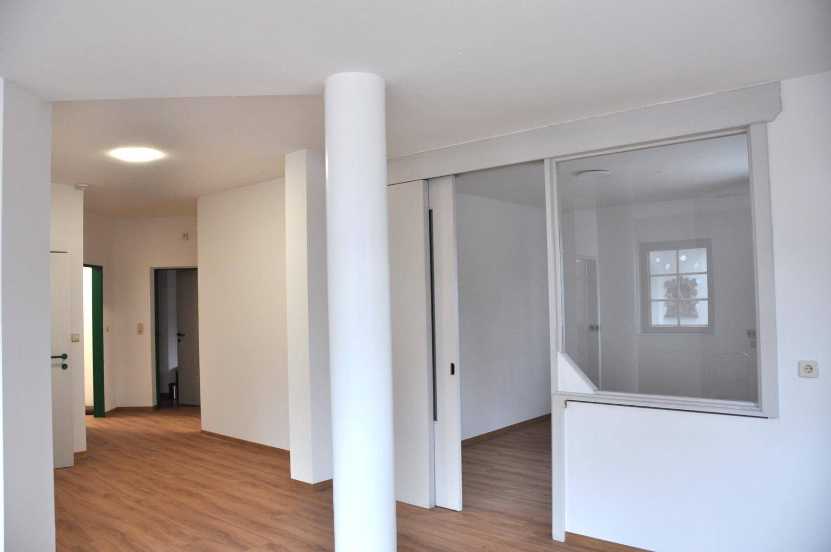 Heller Flur mit Holzfußboden, weißen Wänden und Zugang zu weiteren Räumen.
