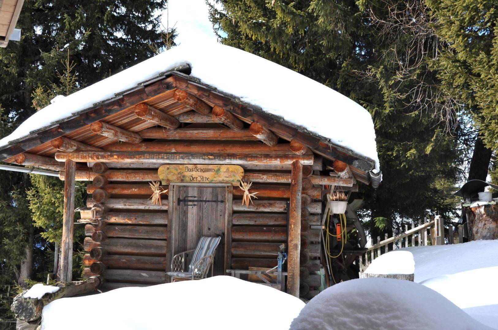 Rustikale Holzhütte im Schnee, umgeben von Tannenbäumen, mit traditioneller Dekoration.