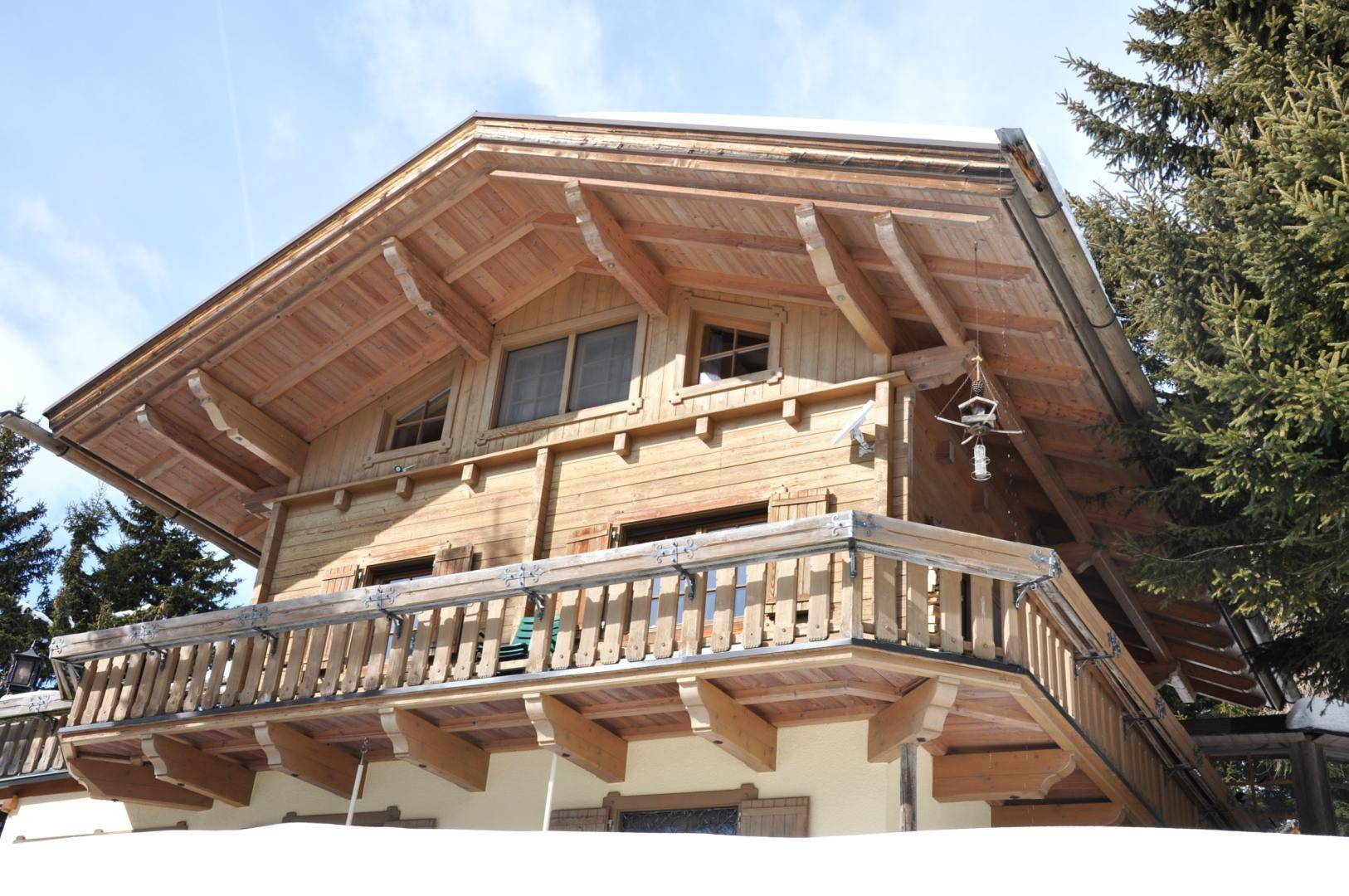 Traditionelles Holzchalet mit Satteldach und Balkonen, umgeben von verschneiten Tannenbäumen.