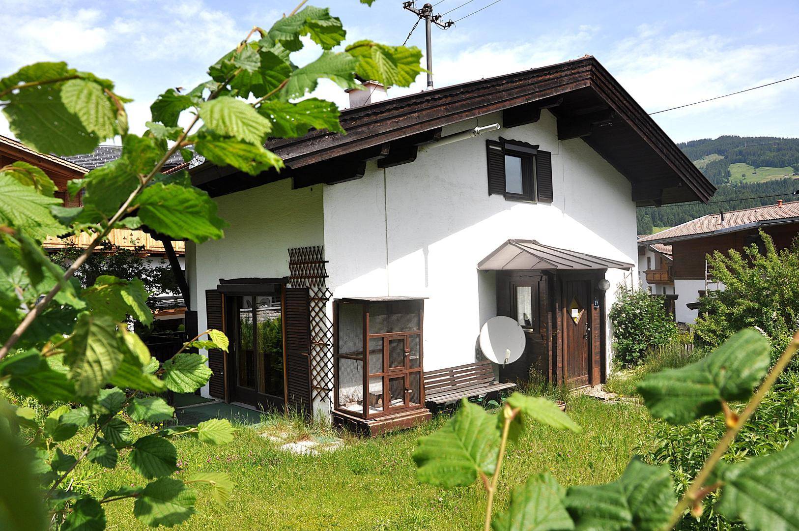 Alpines Haus mit weißer Fassade, Holztür und einem grünen Vorgarten unter blauem Himmel.