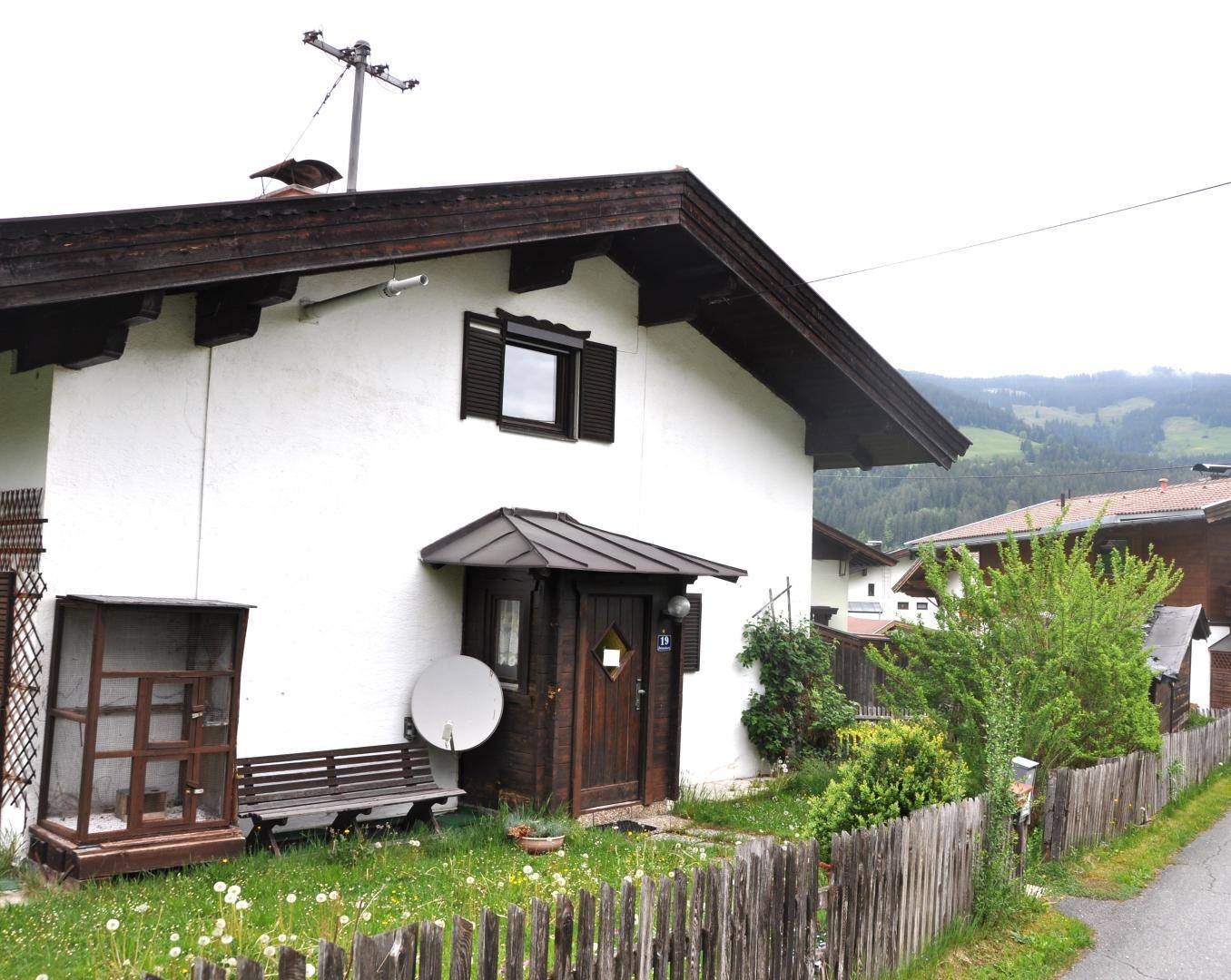 Eingangsbereich eines traditionellen Hauses mit Holztür, kleiner Bank und einem gepflegten Vorgarten.