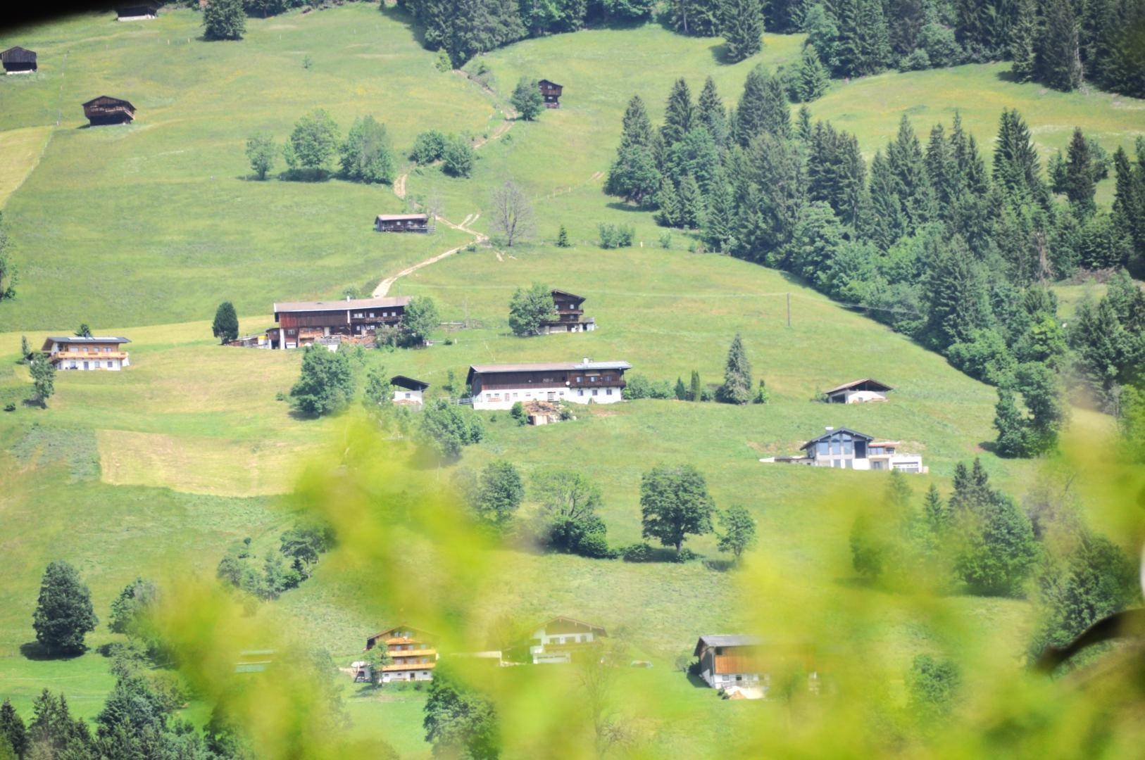 Panoramablick auf eine weite grüne Hügellandschaft mit verstreuten Häusern und Wäldern.