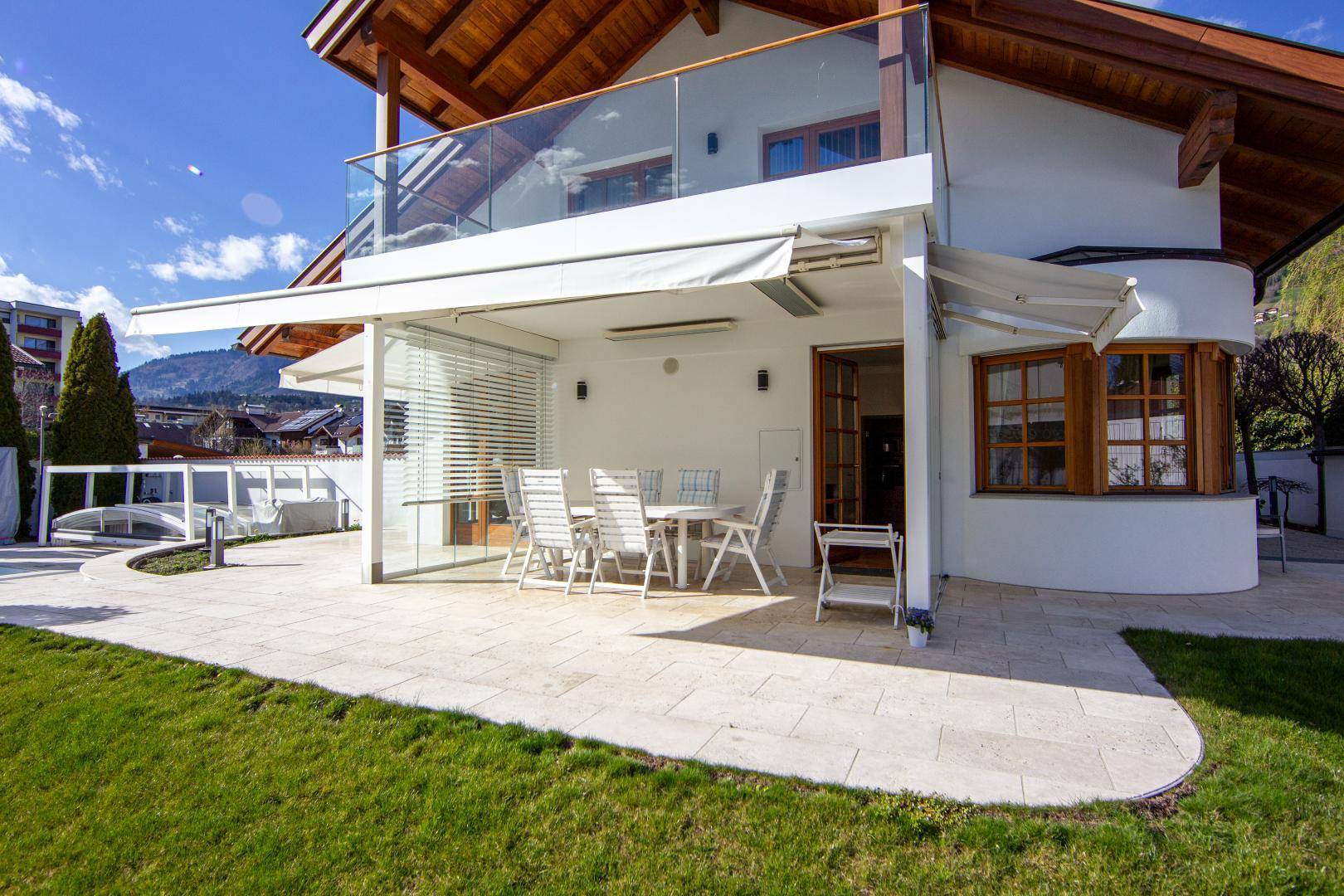 Geräumige, gepflasterte Terrasse mit Esstisch und Stühlen, teilweise überdacht und mit Markise.