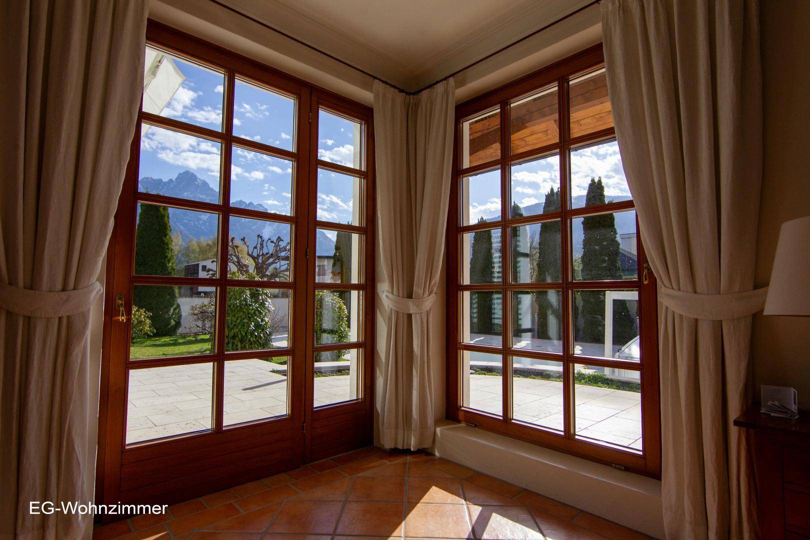 Große Fenster im Wohnzimmer bieten einen weiten Blick auf die Berge und den gepflegten Garten.