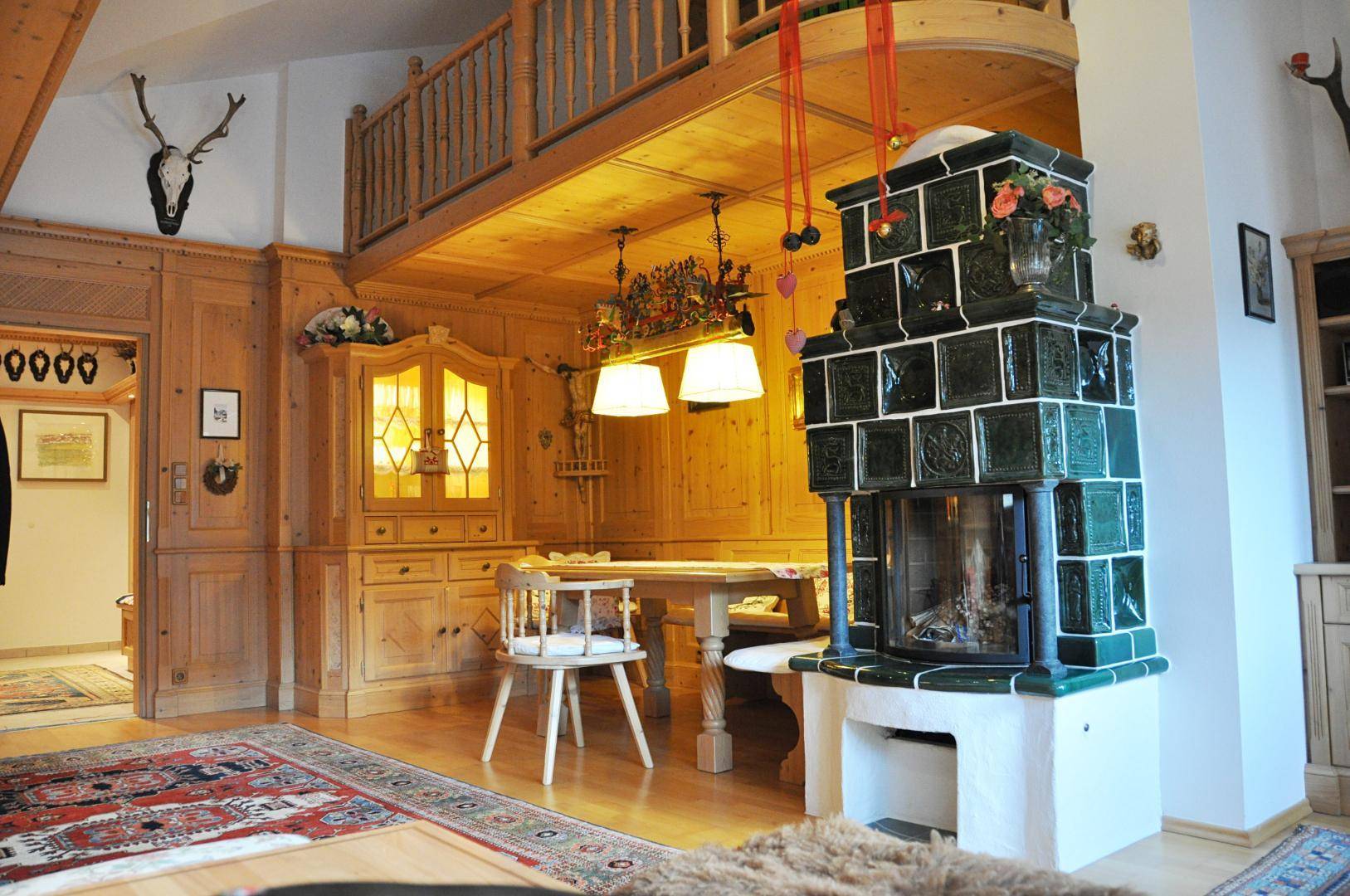 Gemütlicher Wohn-Essbereich im alpinen Stil mit Kachelofen, Holzvertäfelung und einer Galerie.