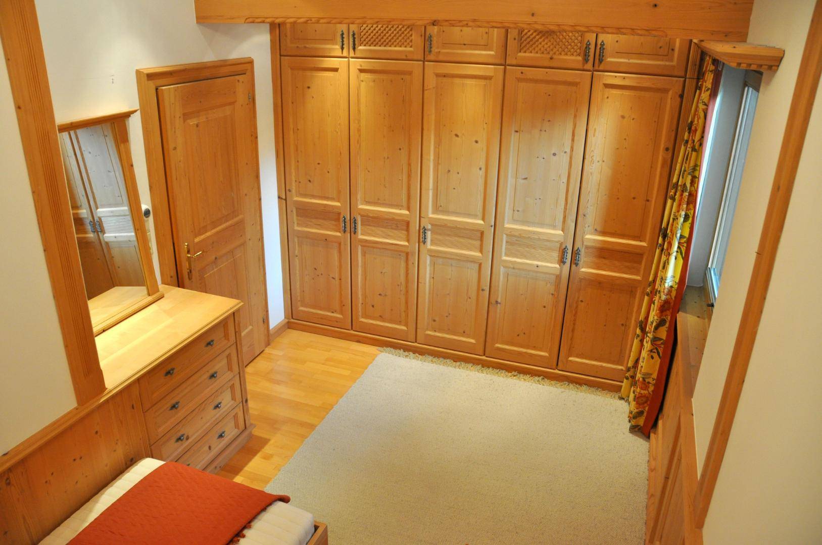 Schlafzimmer mit maßgefertigten Holzschränken, einer Kommode und einem Teppichboden.