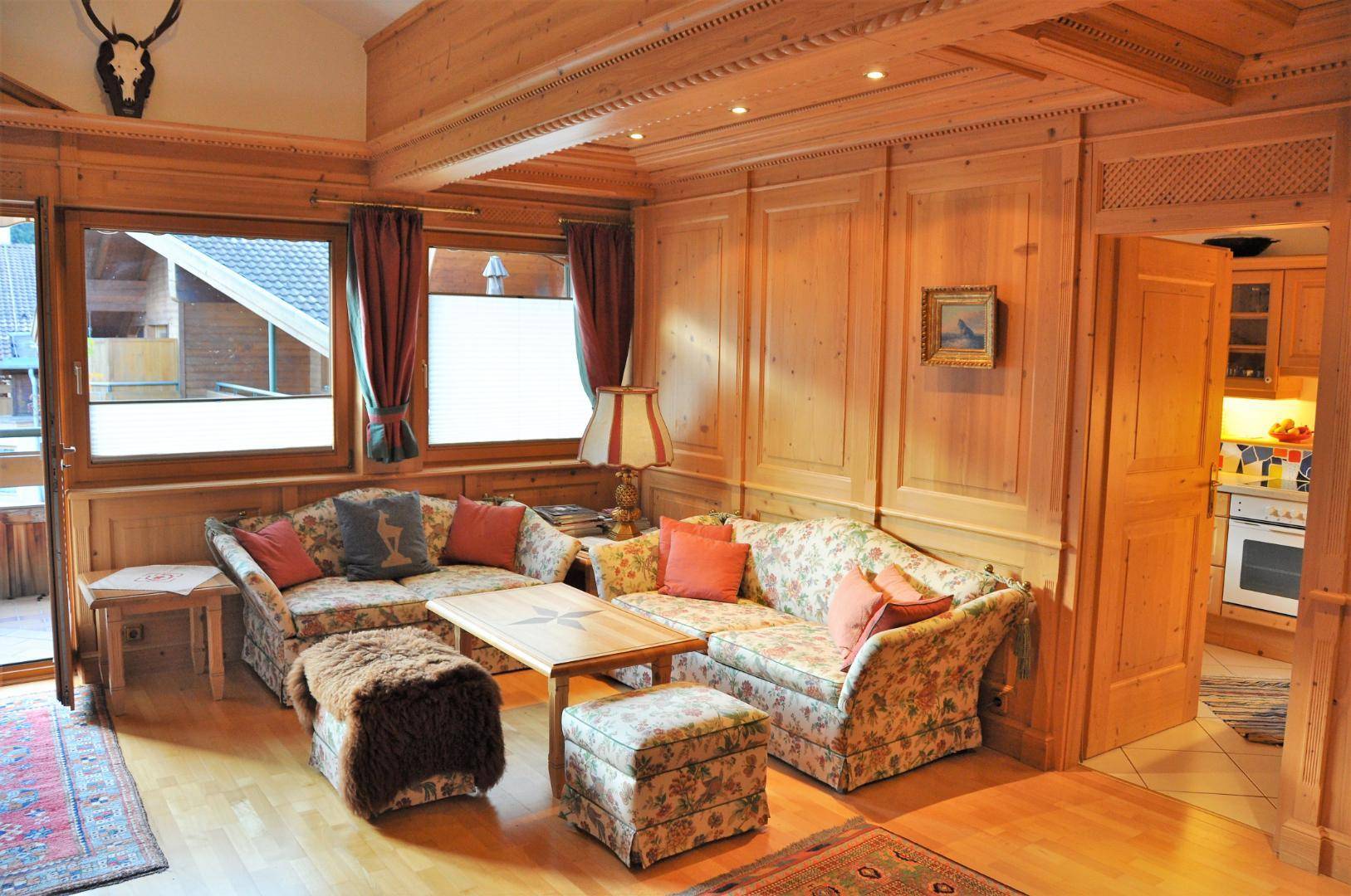 Gemütliches Wohnzimmer mit Holzvertäfelung, floralen Sofas und Blick in die angrenzende Küche.
