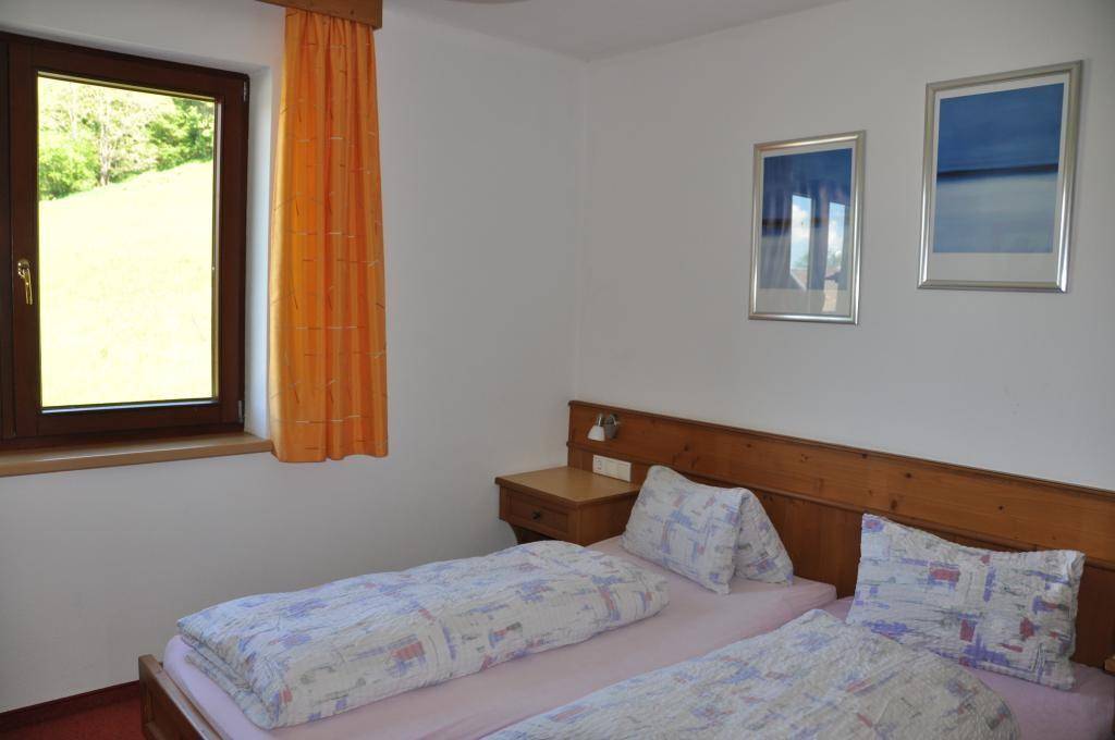 Helles Schlafzimmer mit zwei Einzelbetten, Holzdetails und einem Fenster mit Blick ins Grüne.