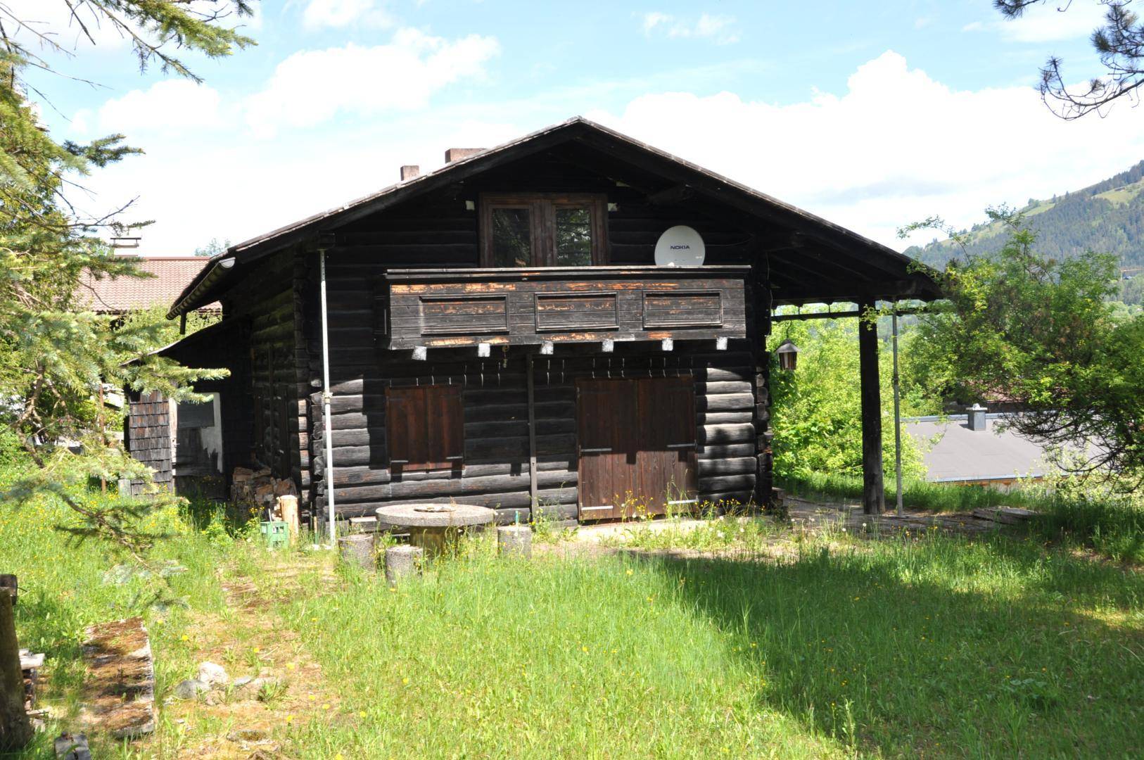 Rustikales Holzhaus mit Balkon und umgebender Wiese in ländlicher Umgebung.