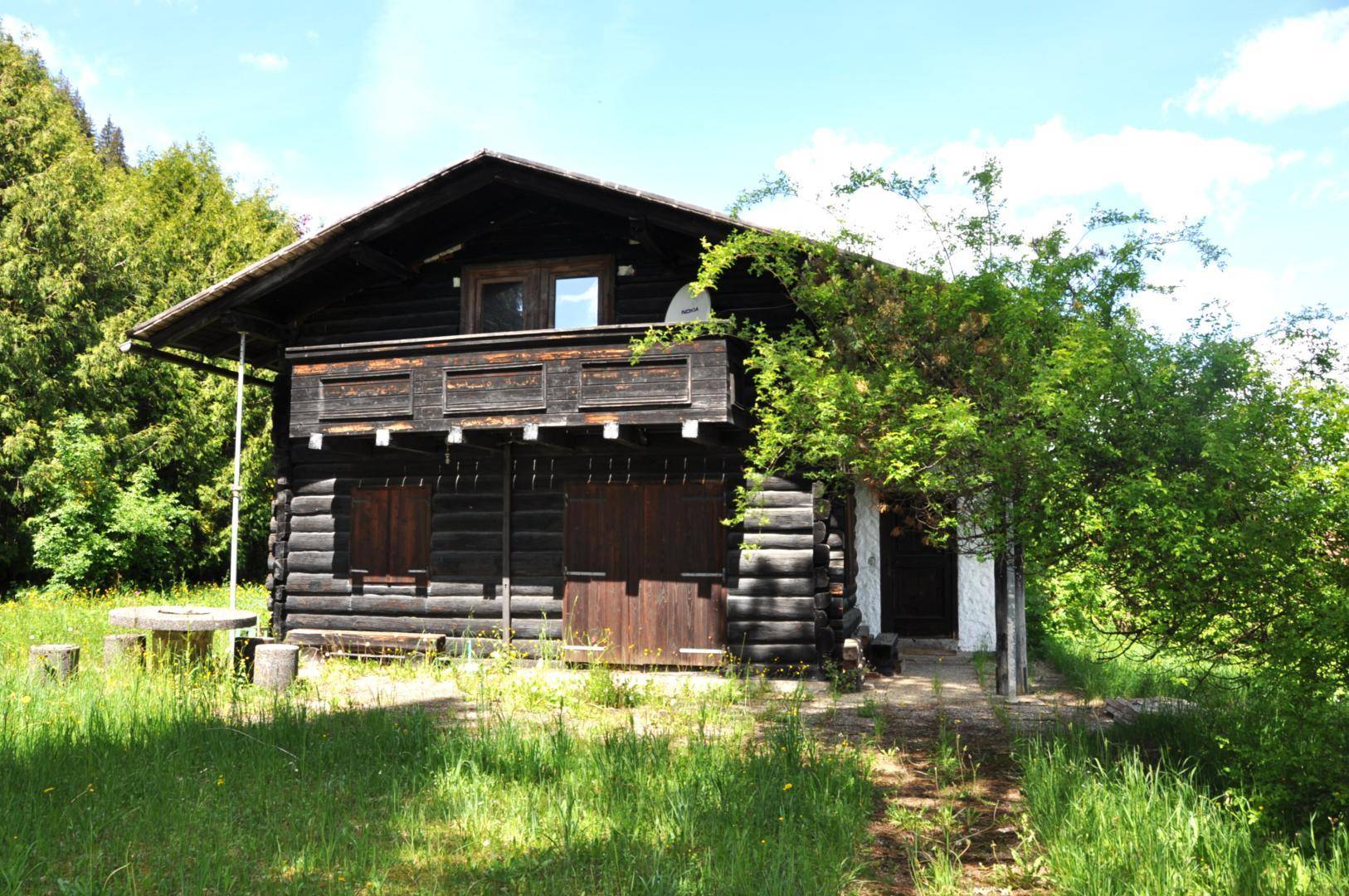 Altes Holzhaus im Chalet-Stil, umgeben von üppiger Natur und Bäumen.