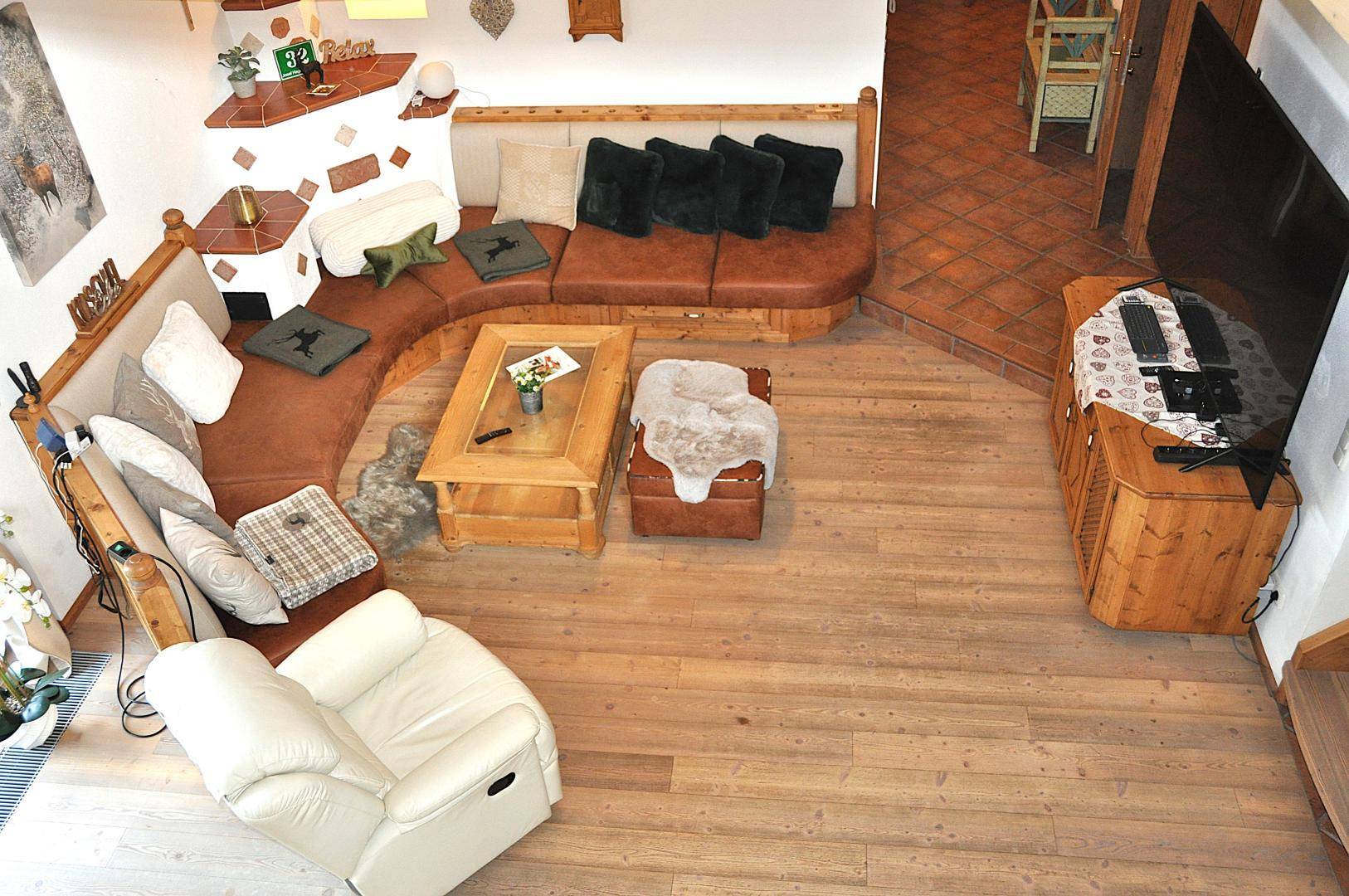 Gemütliches Wohnzimmer mit Ecksofa, Holzboden und traditionellem Kachelofen.