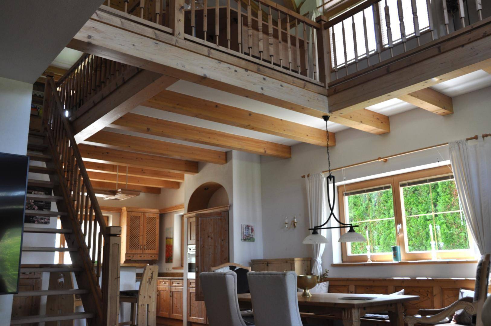 Offener Wohn- und Essbereich mit beeindruckenden Holzbalken, hoher Decke und einer Holztreppe zur Galerie.
