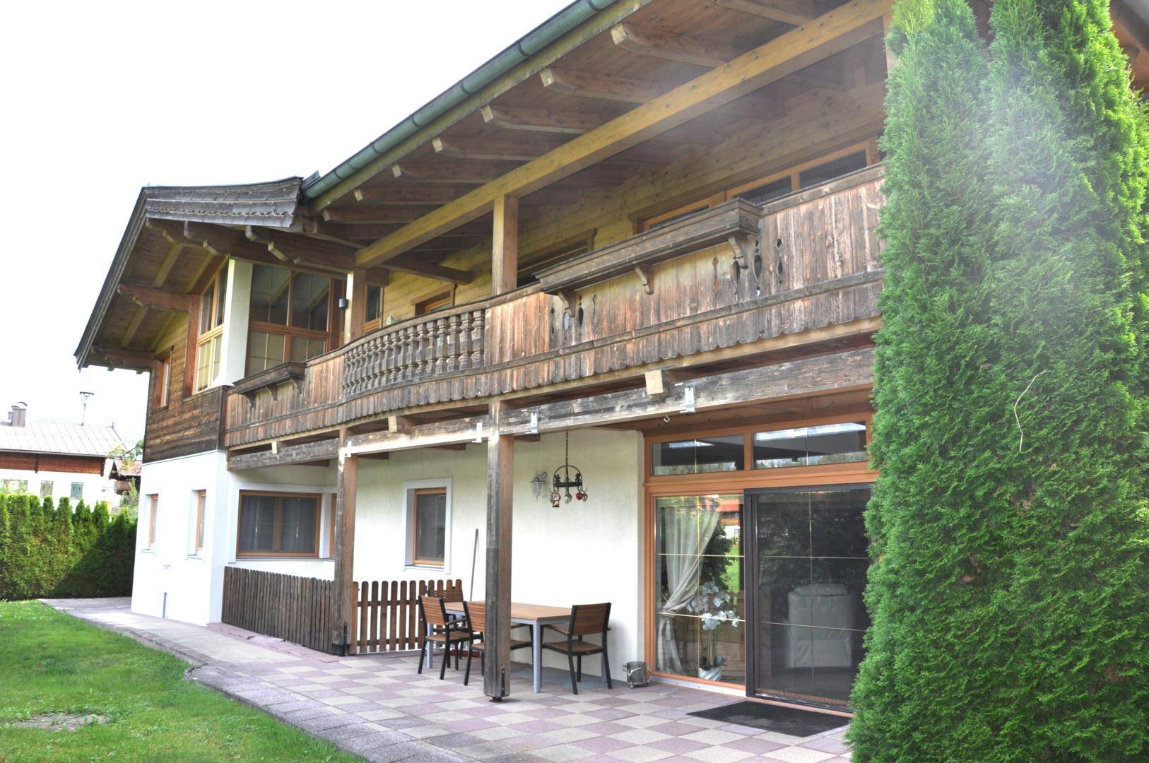 Traditionelles Alpenhaus mit Holzfassade, Balkonen und einer gepflasterten Terrasse mit Sitzgelegenheiten im Garten.
