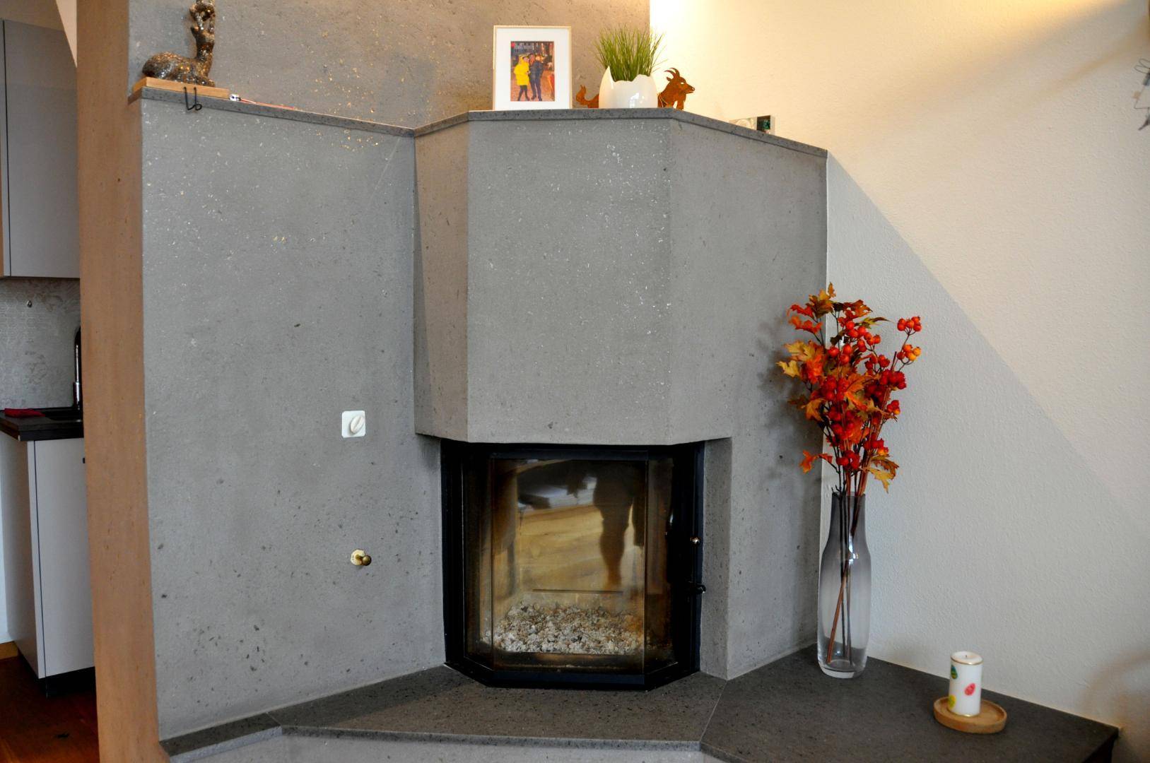 Moderner Eckkamin aus Beton mit dekorativen Elementen und warmem Licht.