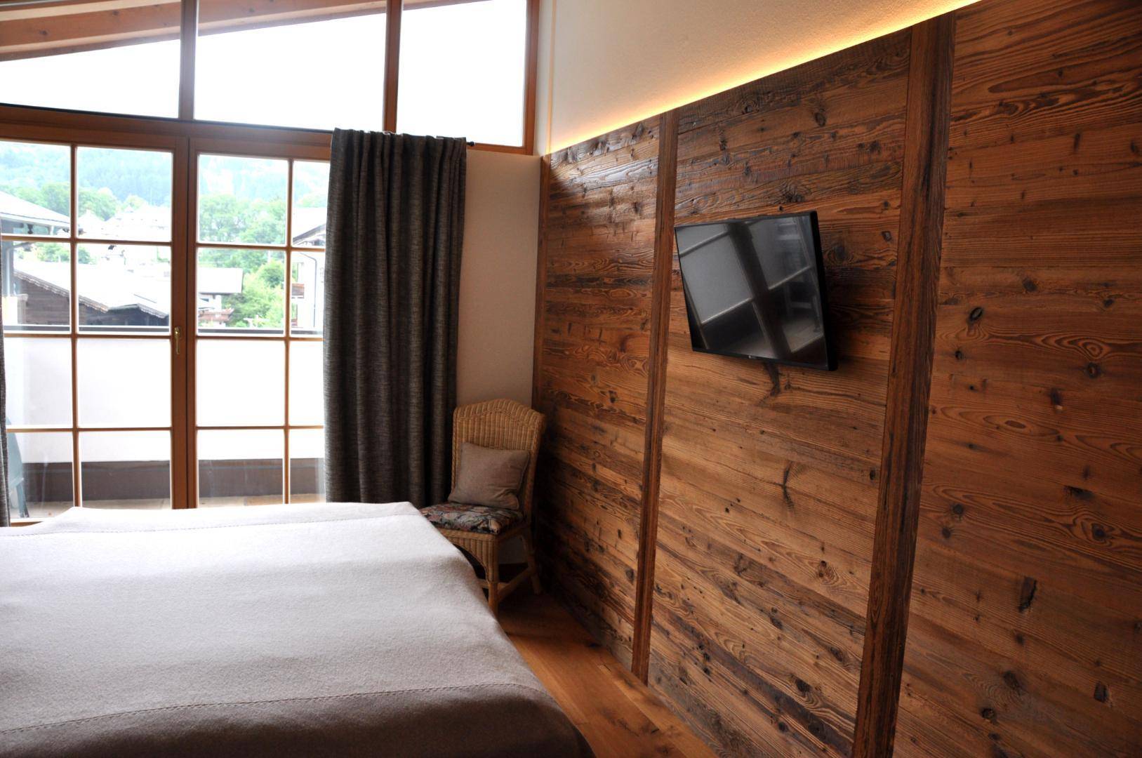 Schlafzimmer mit Holzwandverkleidung, großem Fenster und Blick ins Grüne.