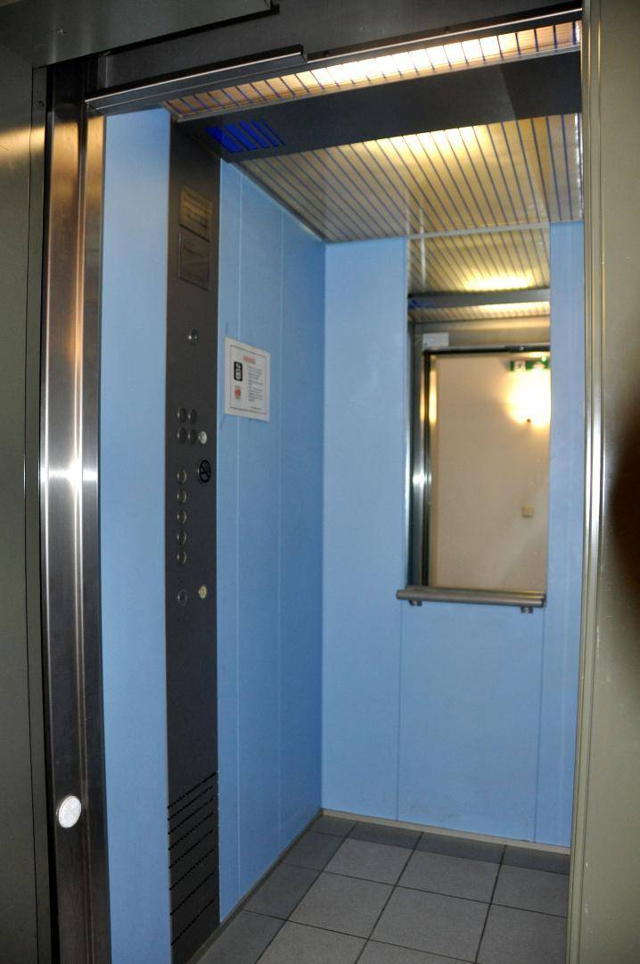 Innenansicht eines Aufzugs mit blauen Wänden und einem Spiegel.