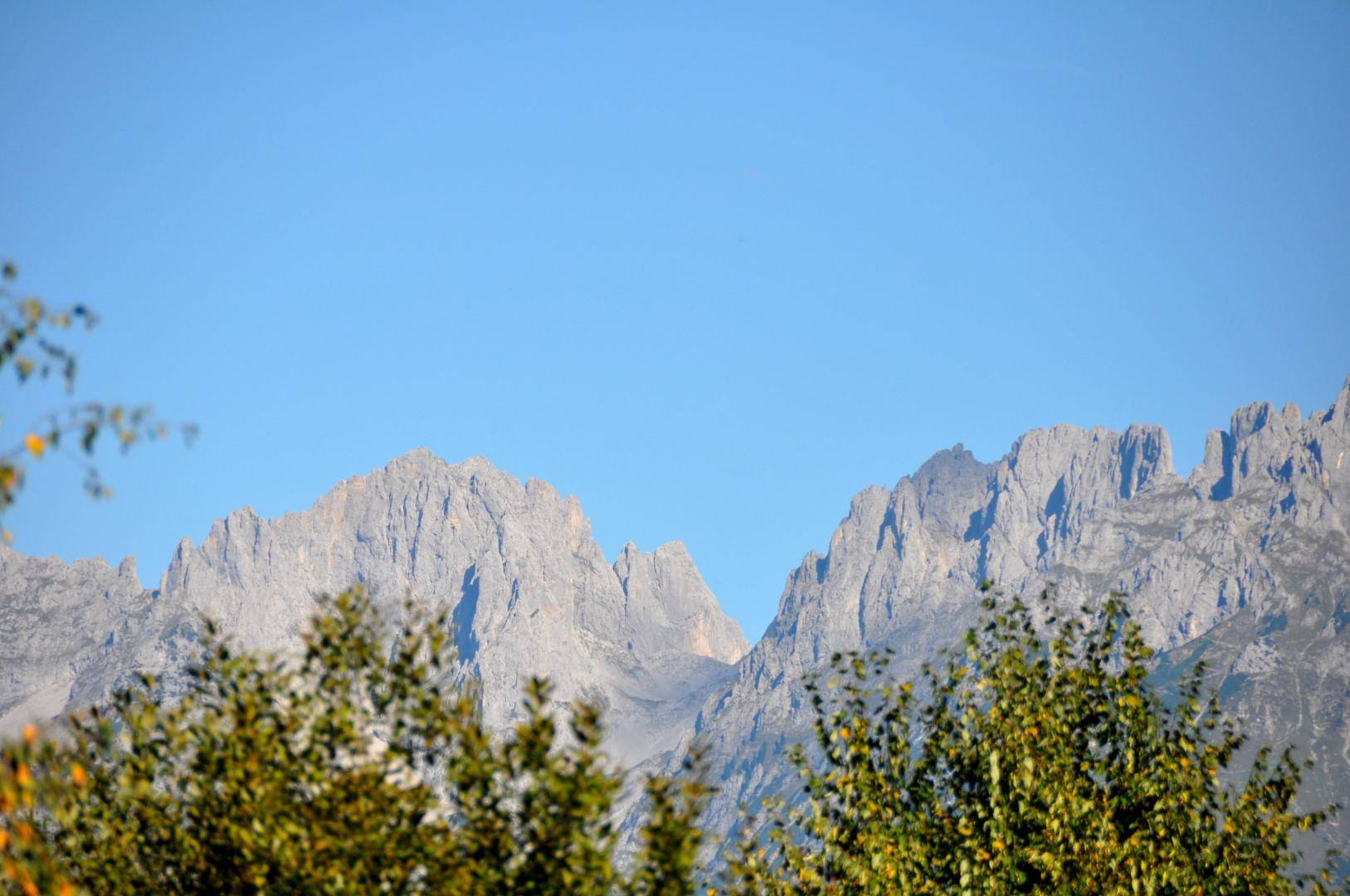 Beeindruckende Berglandschaft mit schroffen Gipfeln und klarem Himmel über grünen Bäumen.