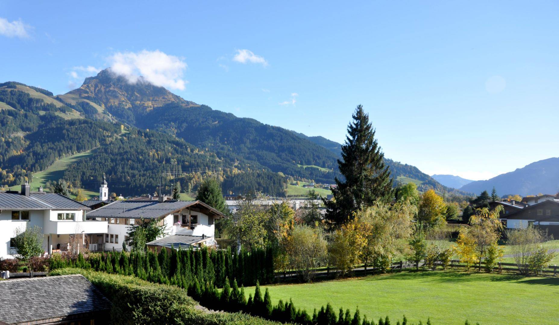 Weitläufiger Blick auf die umliegende Berglandschaft mit grünen Wiesen und vereinzelten Häusern.