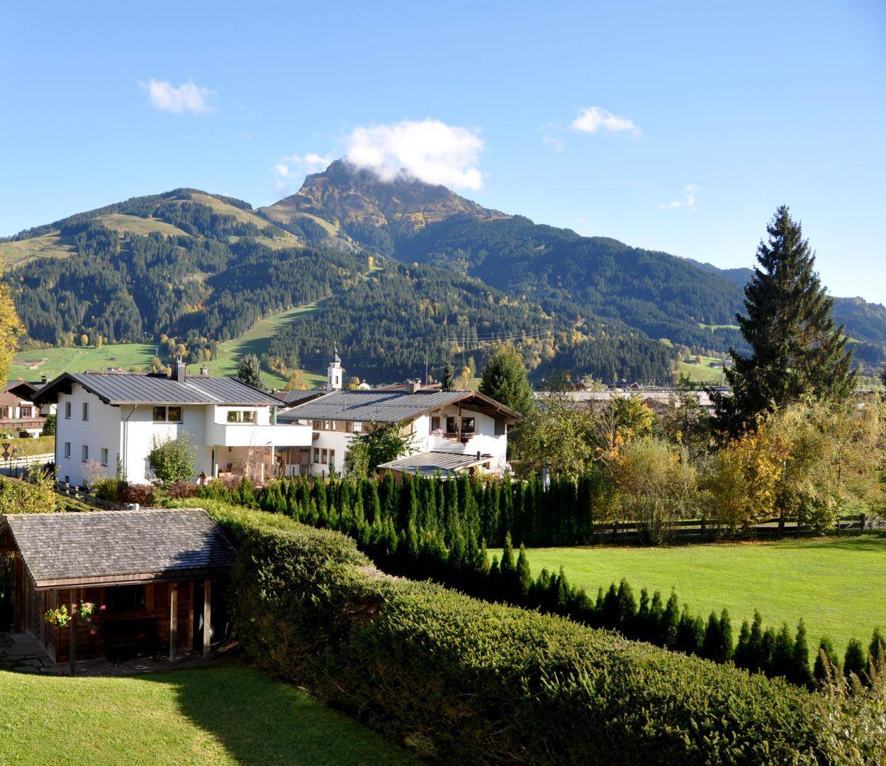 Malerische Landschaft mit Bergen, grünen Wiesen und traditionellen Häusern unter blauem Himmel.