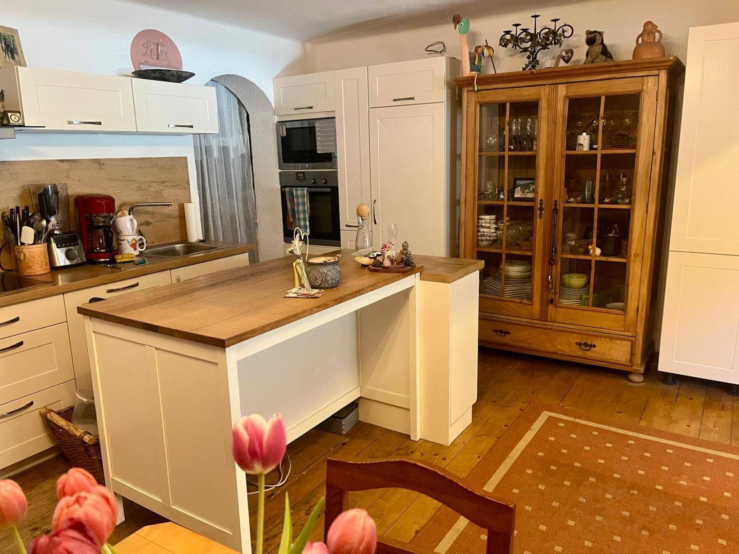 Helle Küche mit weißen Schränken, Holztheke und einem traditionellen Holzschrank für Geschirr.