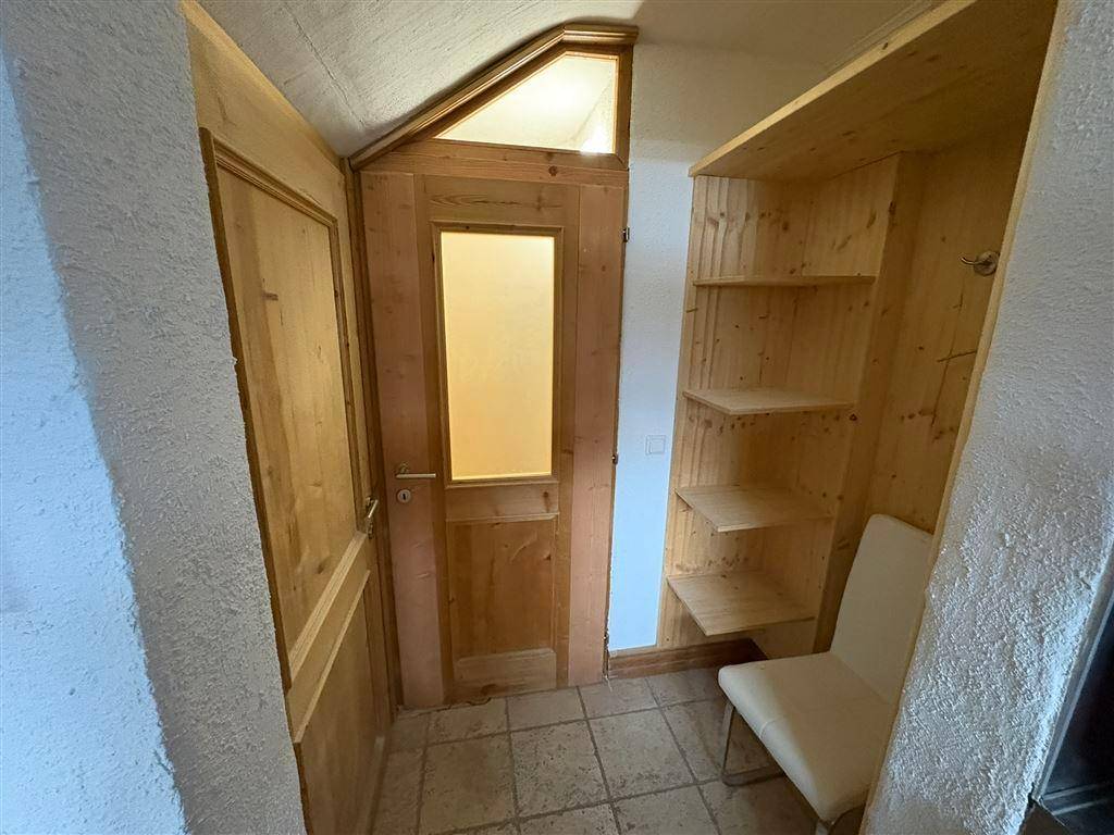 Eingangsbereich mit Holzregalen, einer Sitzgelegenheit und einer Holztür mit Milchglas.