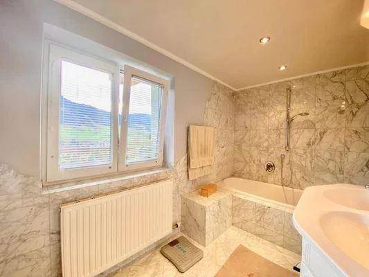 Helles Badezimmer mit Marmorfliesen, Badewanne und Fenster mit Bergblick.