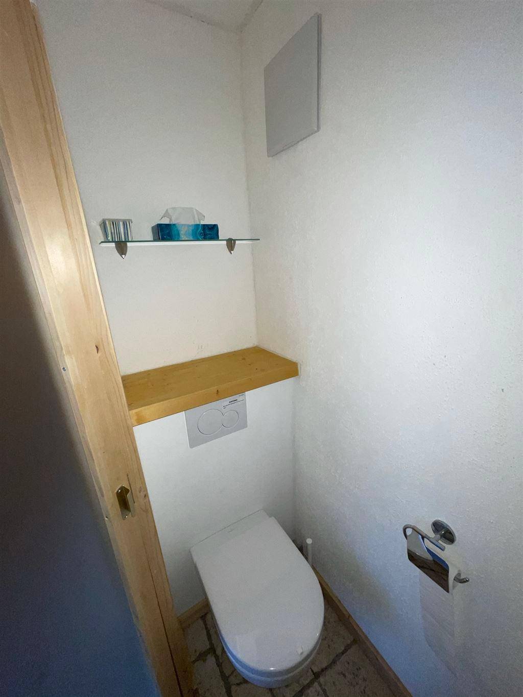 Separates WC mit Toilette, einer Holzablage und Fliesenboden.