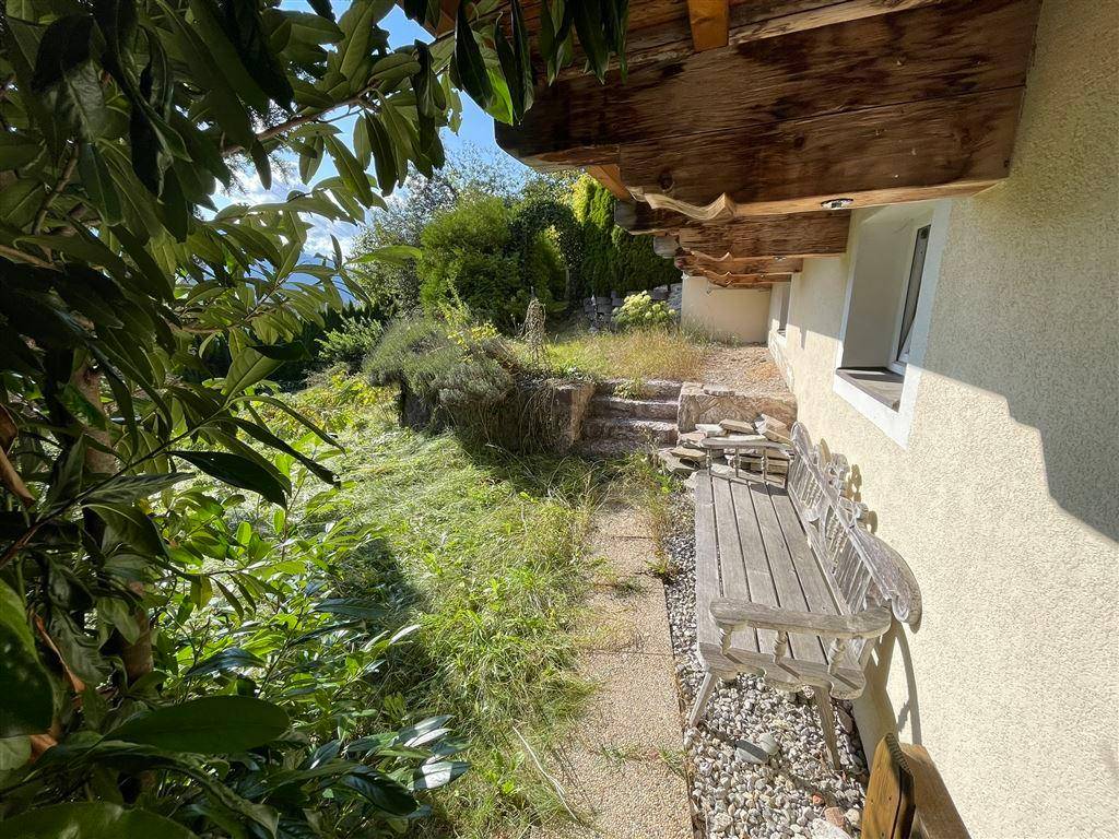 Seitenansicht des Hauses mit rustikaler Holzbank und Blick in die Landschaft.