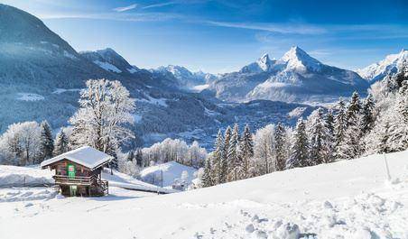 Idyllische Winterlandschaft mit verschneiten Bergen und einem kleinen Holzhaus im Vordergrund.