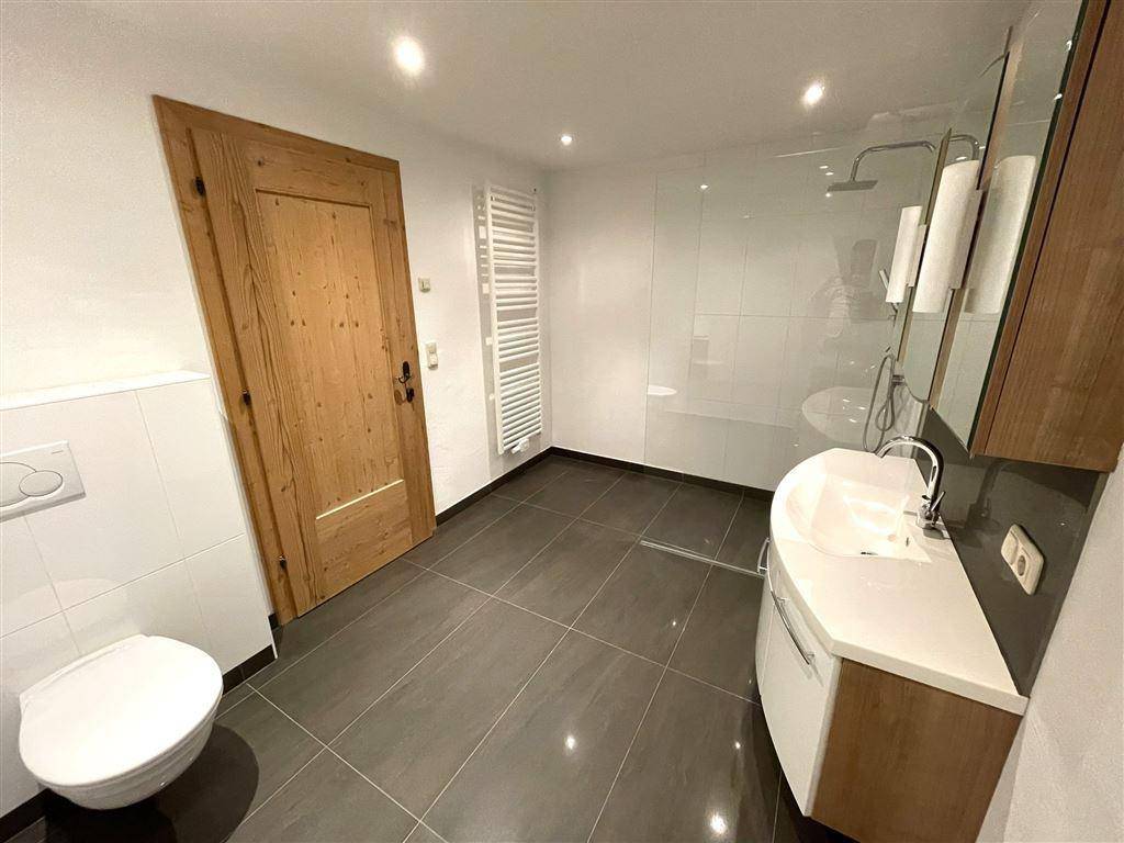 Modernes Badezimmer mit ebenerdiger Dusche, Wand-WC und beheiztem Handtuchhalter.