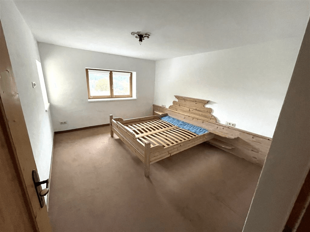 Schlafzimmer mit traditionellem Holzbett und Fenster, das viel Tageslicht hereinlässt.