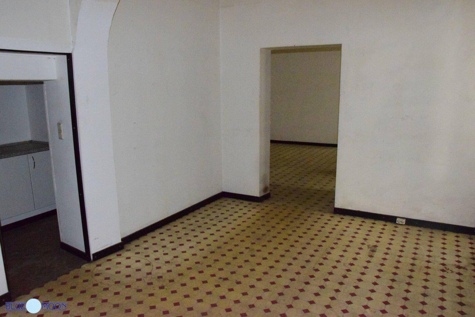 Leerer Innenraum mit gemustertem Fliesenboden, weißen Wänden und mehreren Türöffnungen zu angrenzenden Räumen.