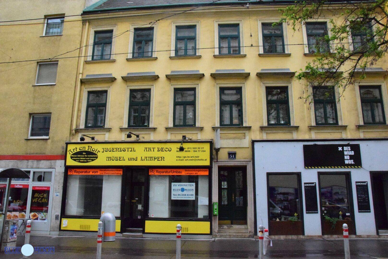 Gesamtansicht der gelben Fassade eines Altbaus mit mehreren Fenstern und einem Ladenlokal im Erdgeschoss.