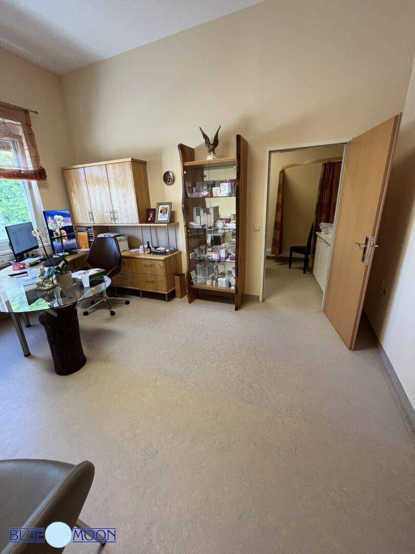 Büro mit Schreibtisch, Vitrine und einem offenen Durchgang zu einem weiteren Raum.