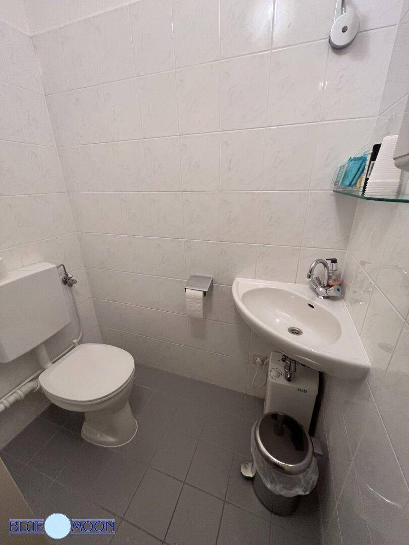 Kleines Badezimmer mit Toilette, Eckwaschbecken und weißen Fliesen an den Wänden.