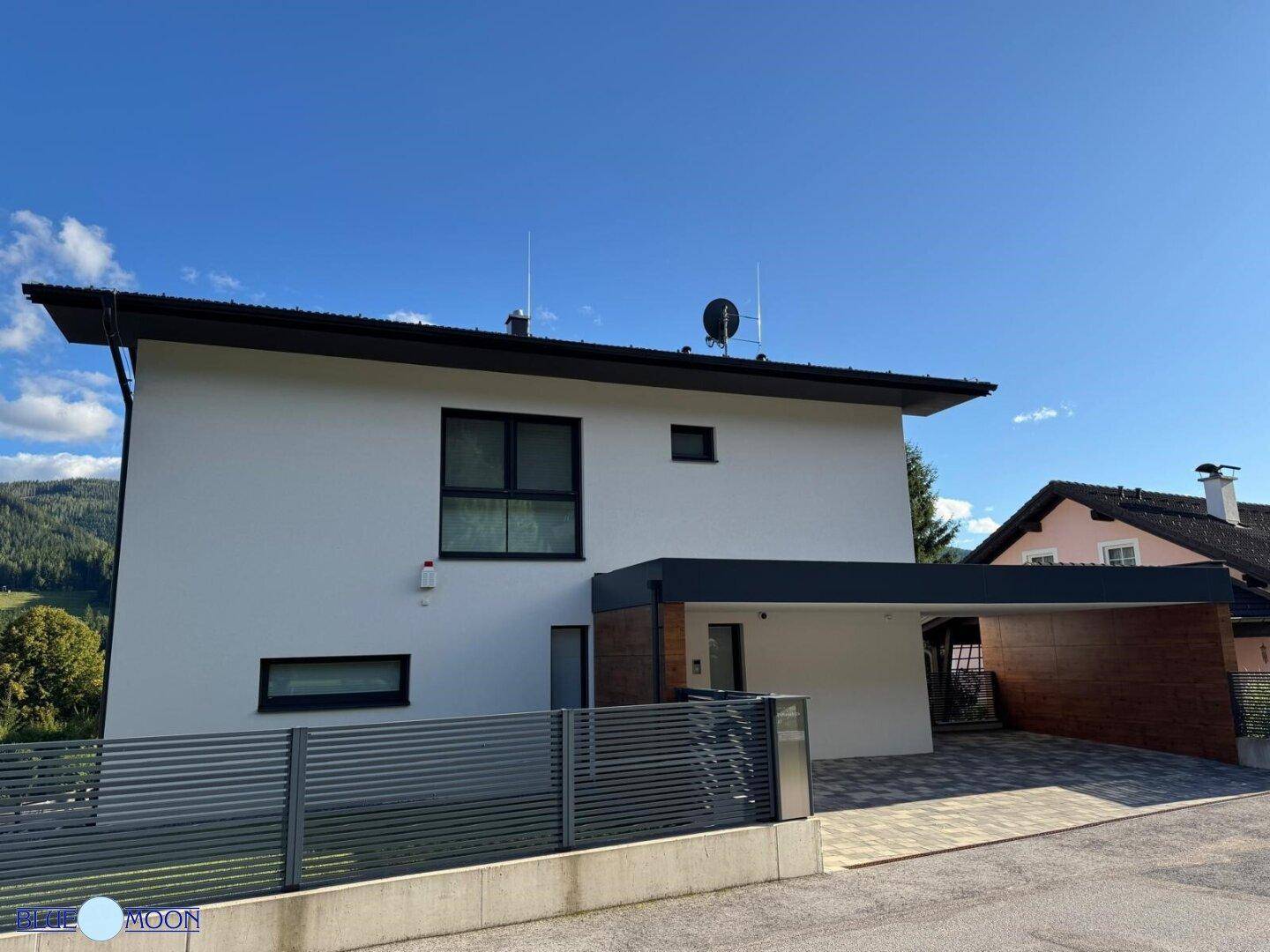 Ansicht des modernen Hauses mit weißer Fassade, dunklem Dach und Carport.