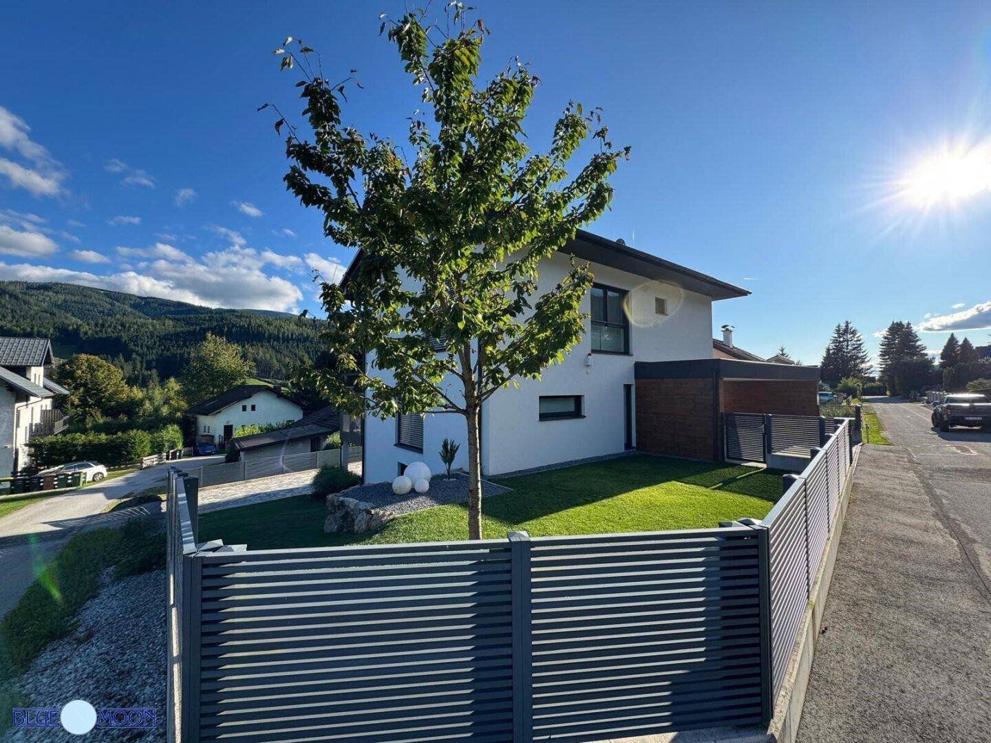 Weitläufiger Blick auf den gepflegten Vorgarten mit Rasen und dem modernen Haus.