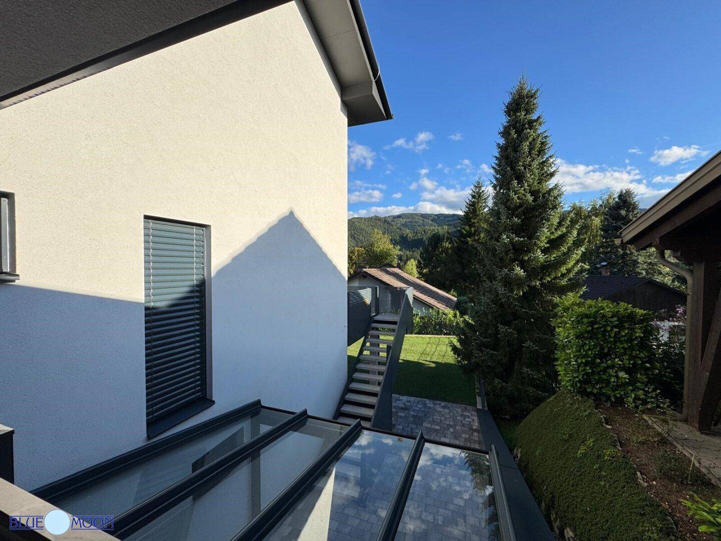 Seitenansicht des Hauses mit Glasdachstruktur und Blick auf die grüne Umgebung.