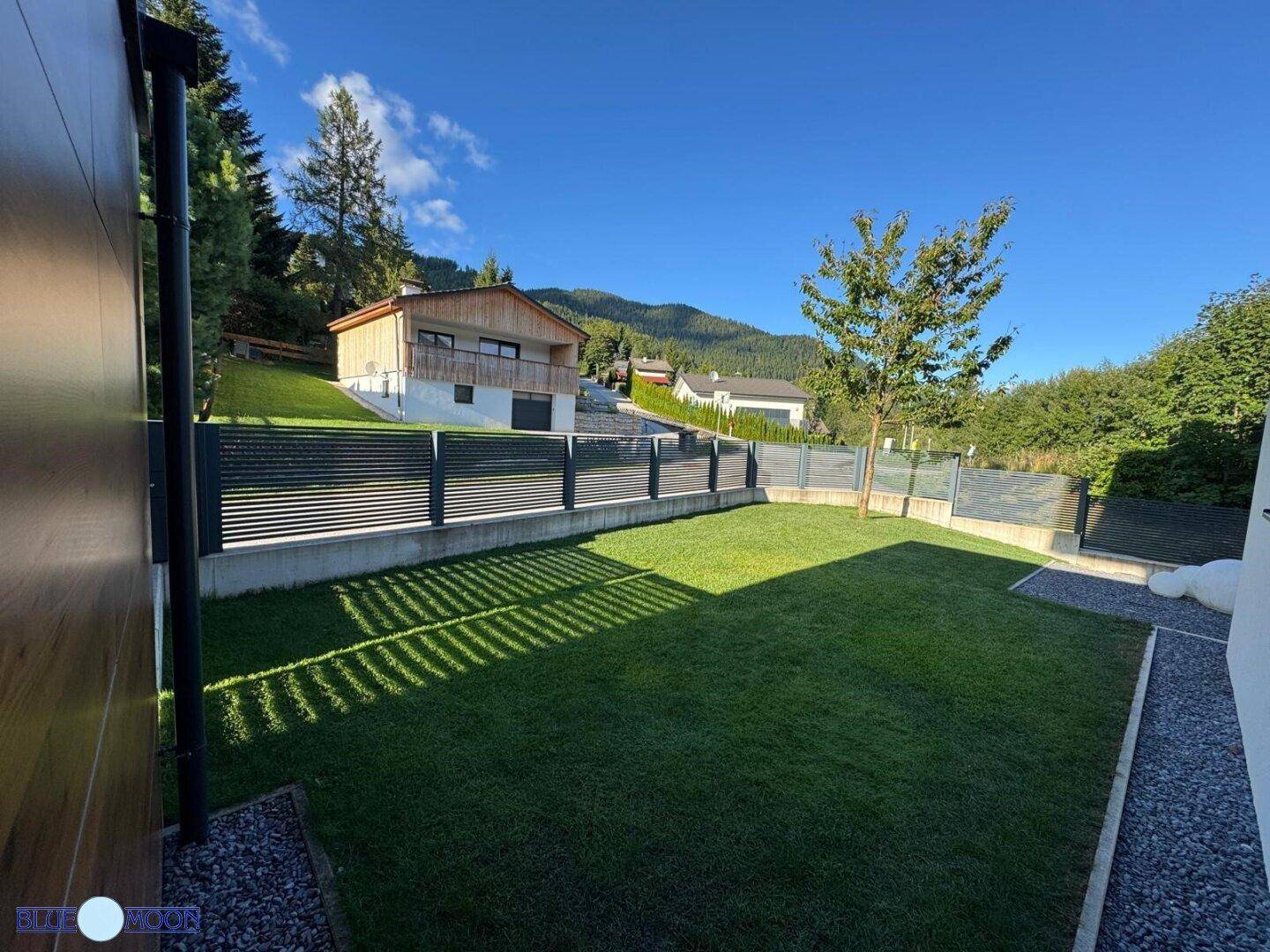 Gepflegter Gartenbereich mit Rasenfläche und moderner Zaunanlage vor bergiger Kulisse.