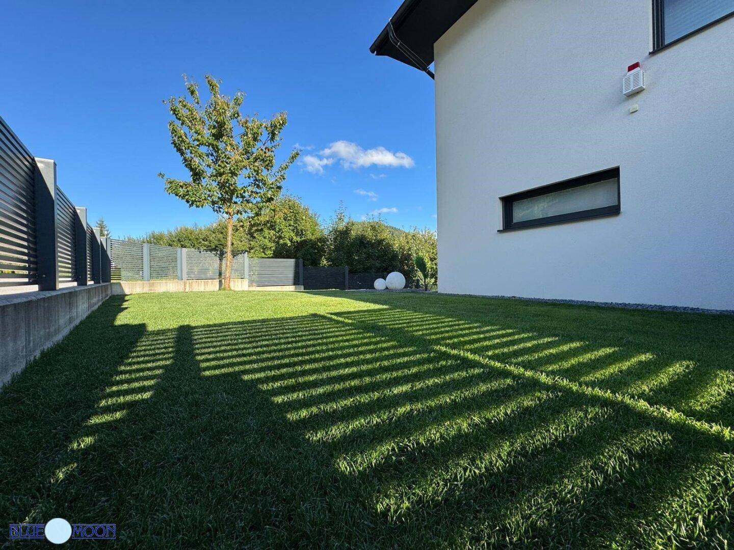 Sonnige Rasenfläche im Garten mit langen Schatten und Blick auf die Umgebung.