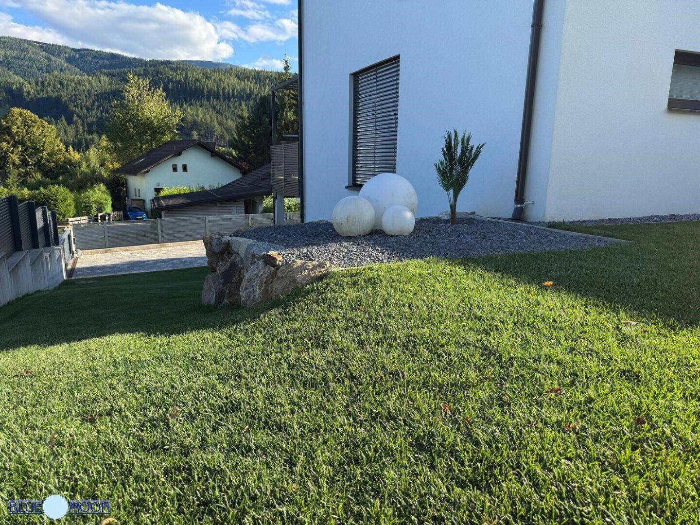 Dekoratives Gartenbeet mit Steinen, weißen Kugeln und gepflegtem Rasenbereich.
