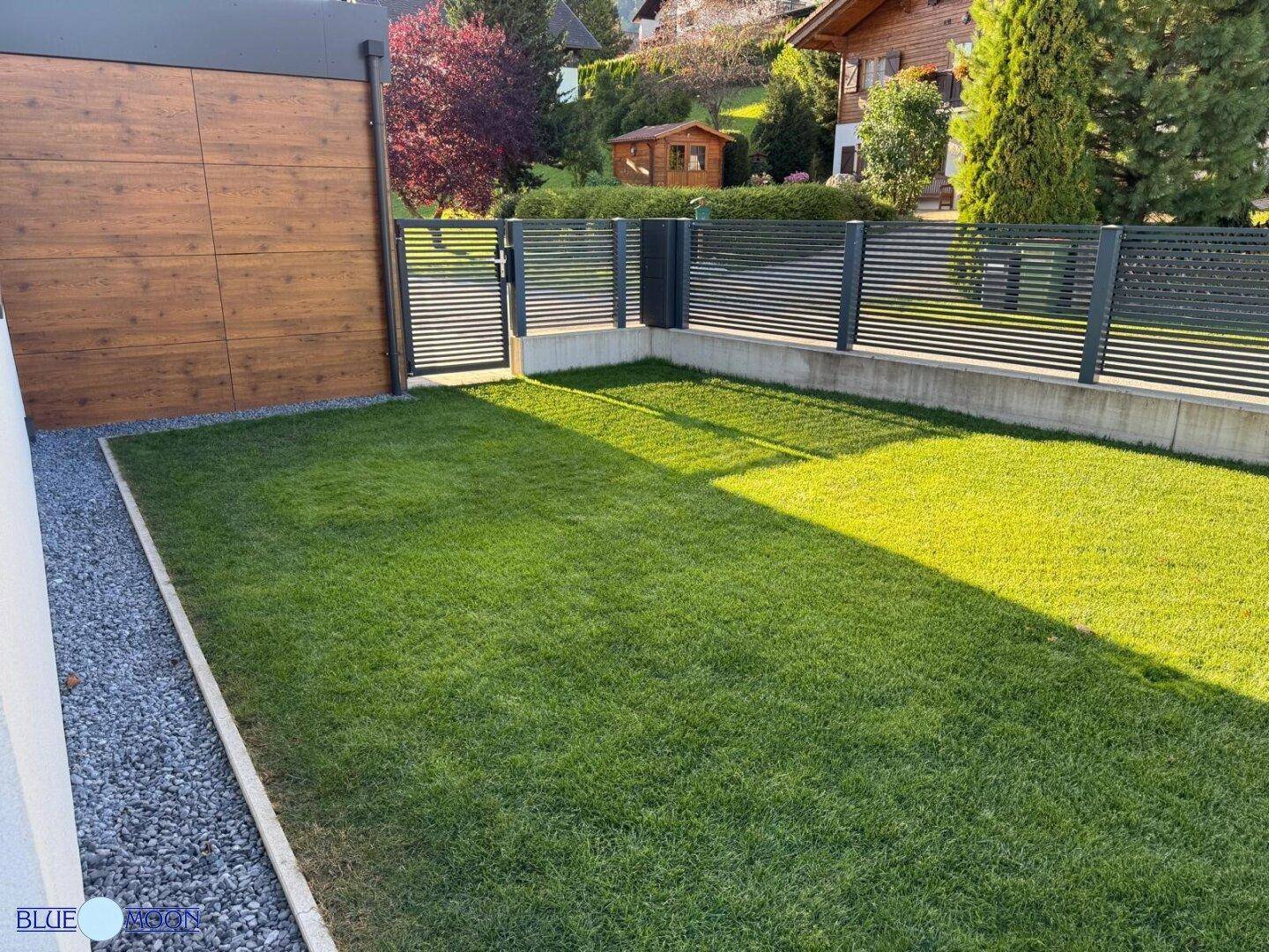 Kleiner, gepflegter Rasenbereich neben dem Haus mit moderner Zaunanlage.