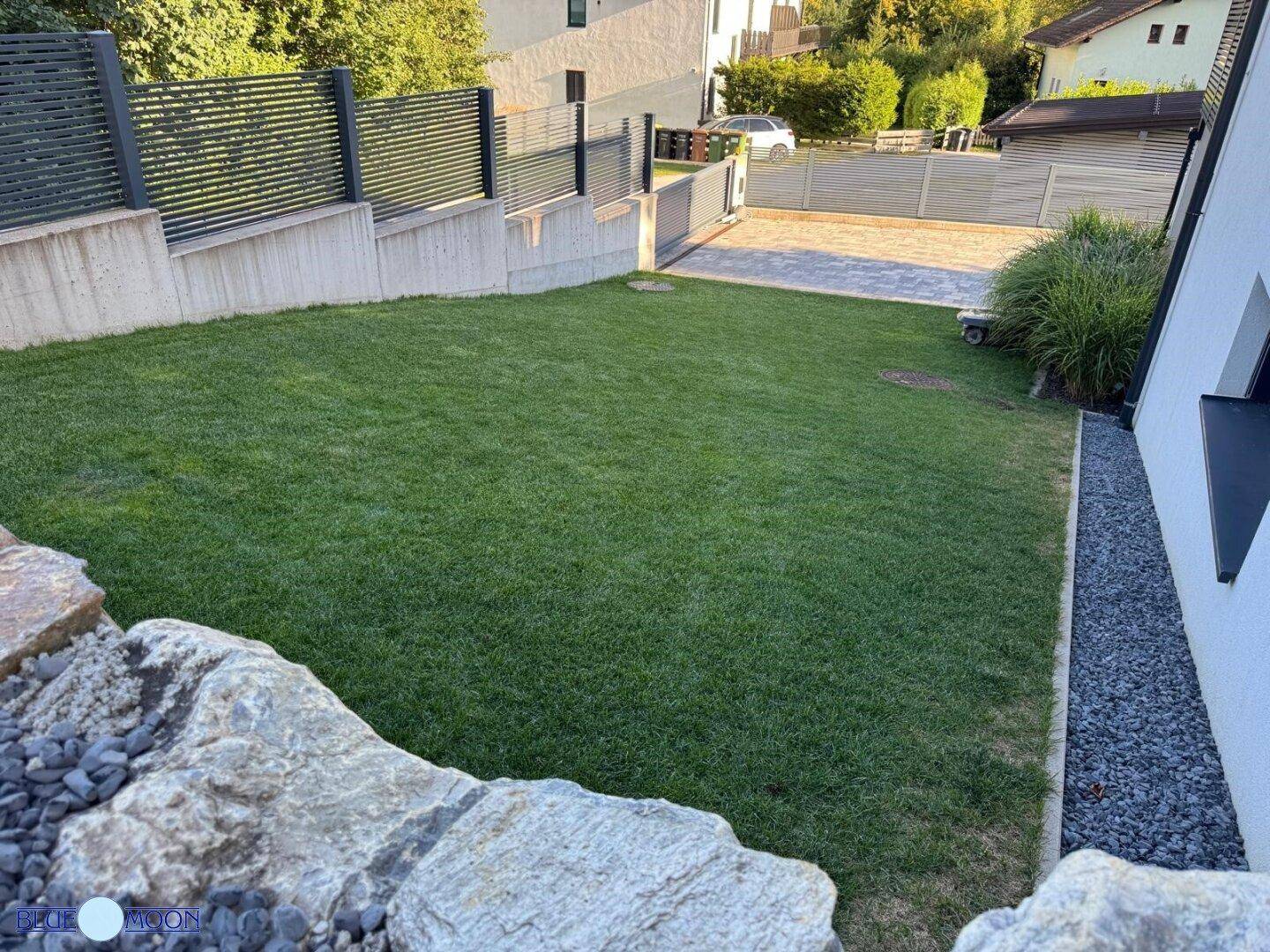 Blick von oben auf den gepflegten Gartenbereich mit Rasen und angrenzender Auffahrt.
