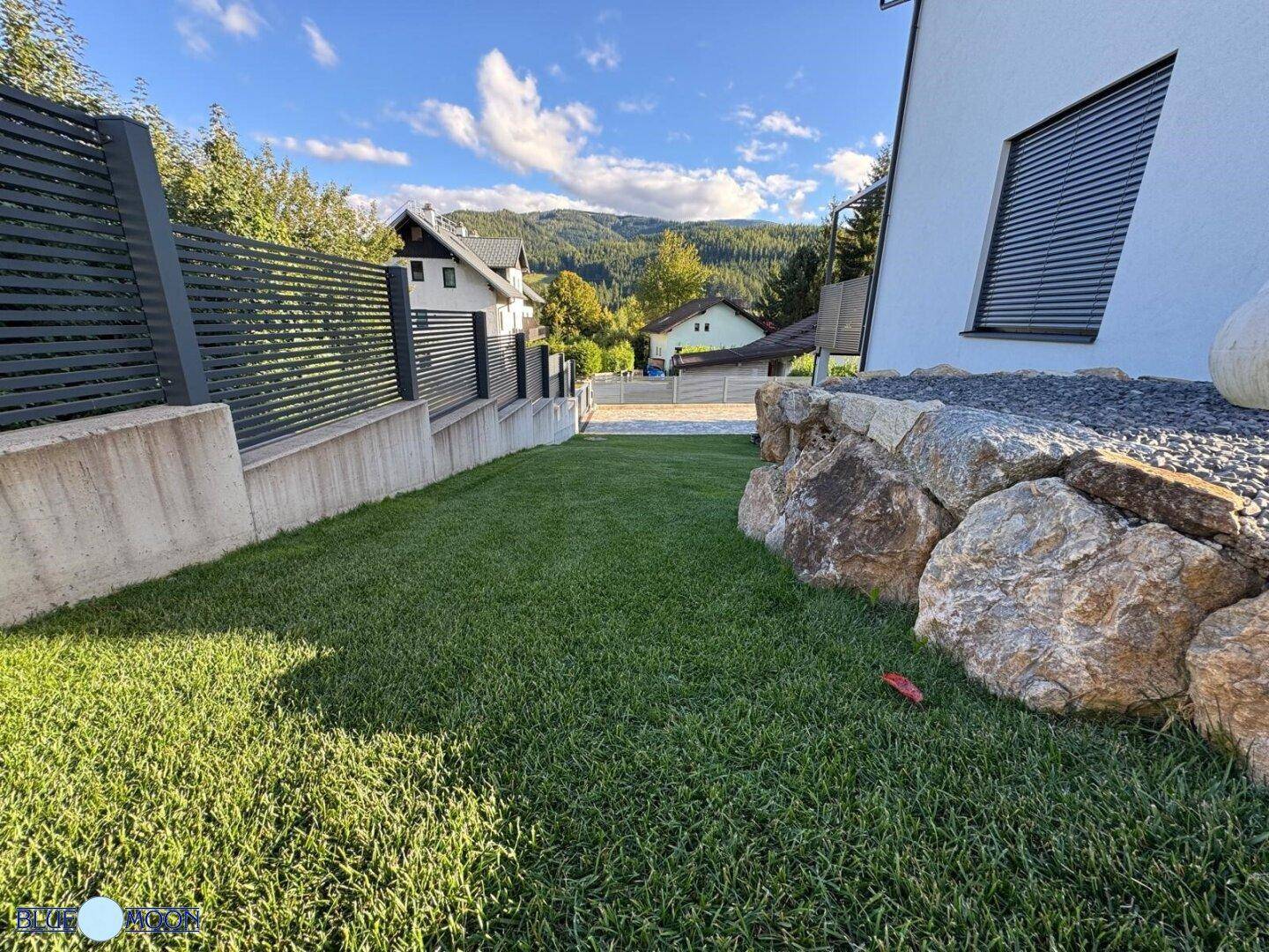 Naturnaher Gartenbereich mit großen Felsen, gepflegtem Rasen und grüner Umgebung.