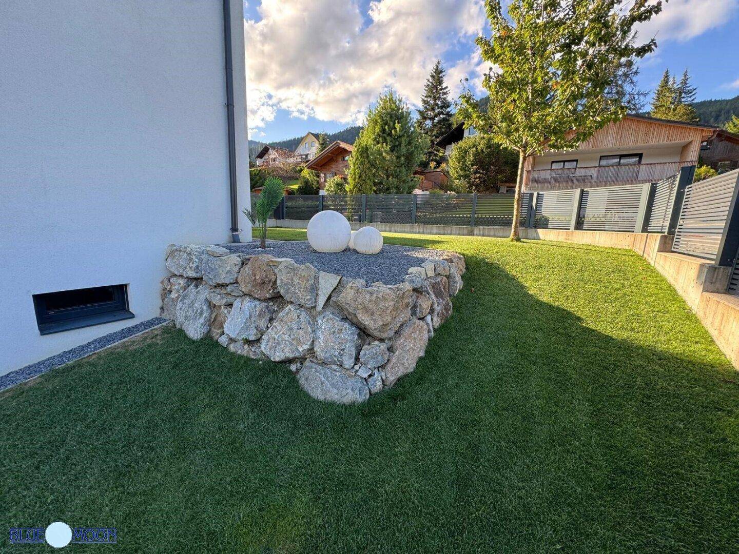 Attraktive Steinmauer mit dekorativen Kugeln und gepflegtem Rasen im Garten.