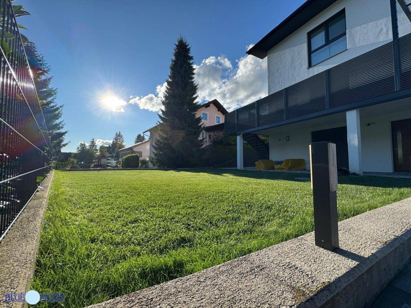 Sonnige Rasenfläche vor dem modernen Haus mit Blick auf die umliegende Natur und Berge.
