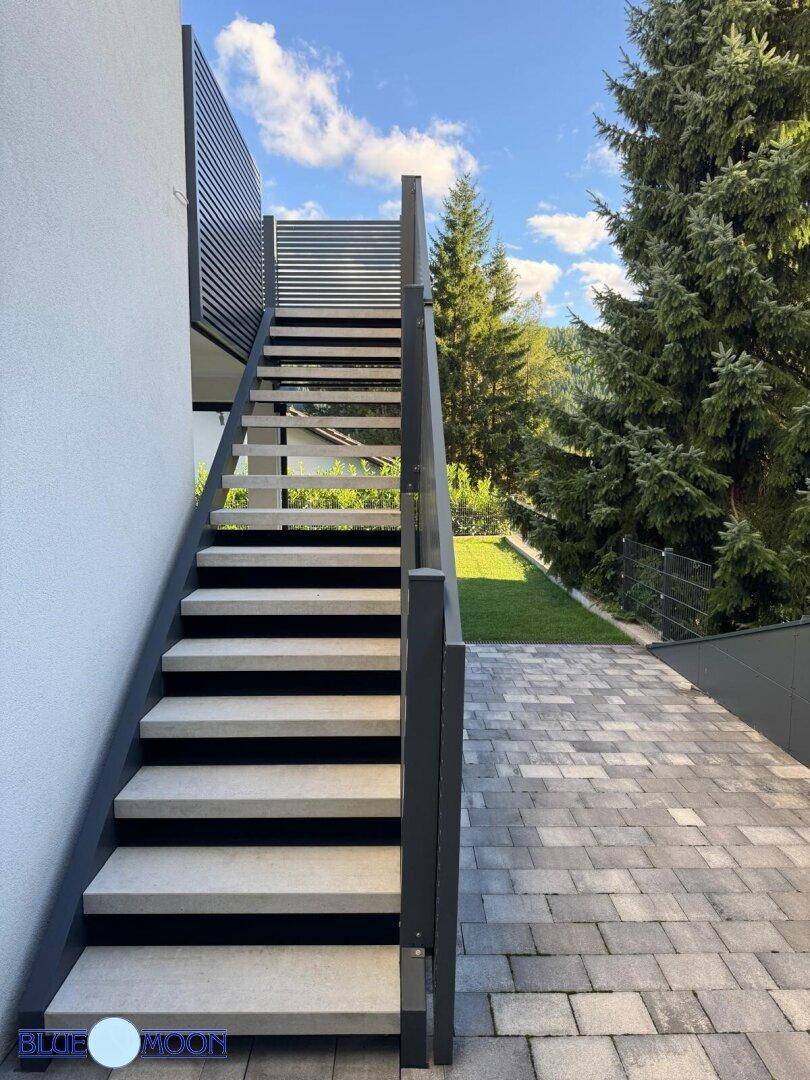 Moderne Außentreppe mit Steinstufen und gepflastertem Weg, umgeben von Grünflächen.