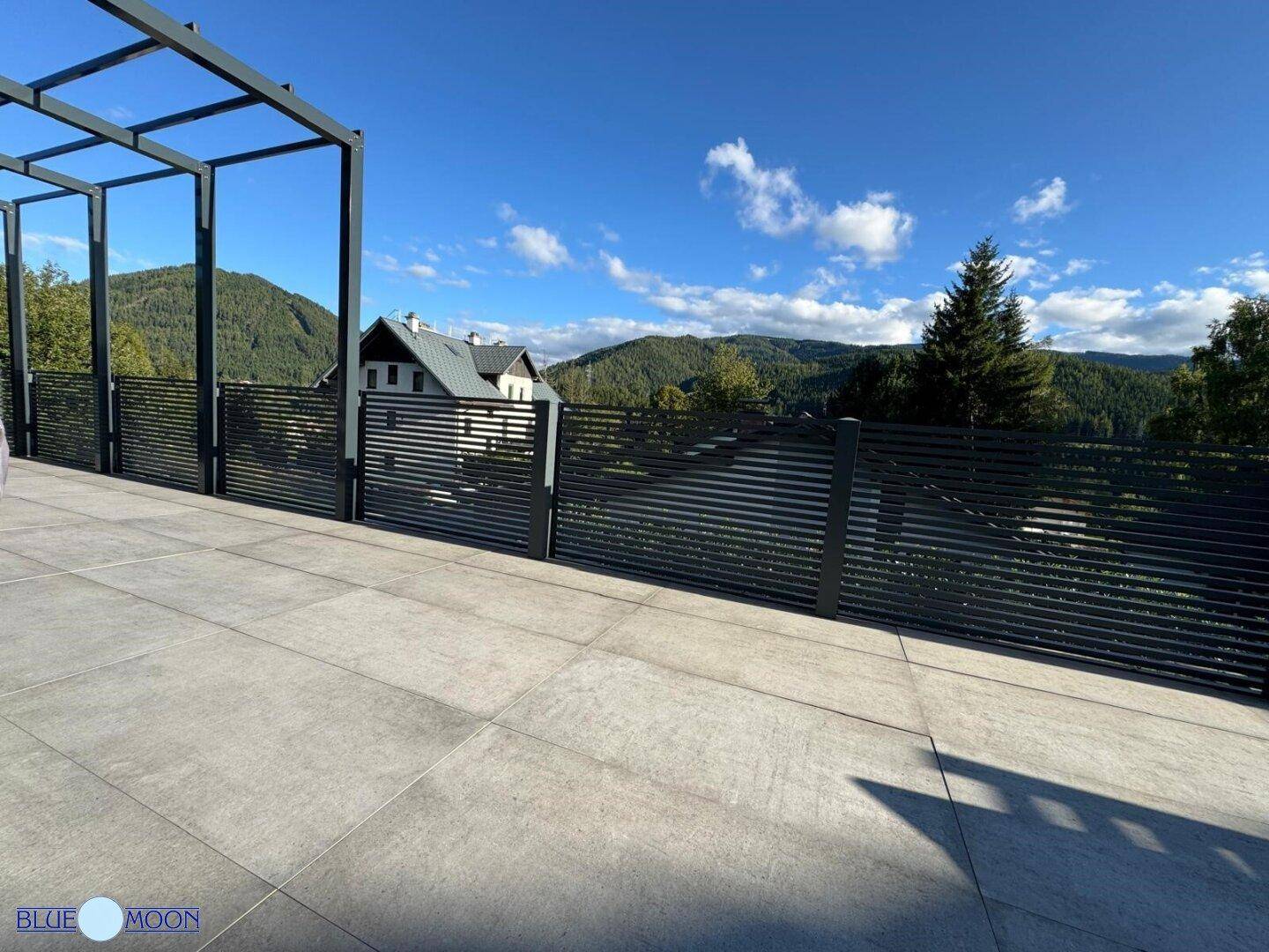 Große, geflieste Terrasse mit Pergola-Struktur und weitem Blick auf die Berge.