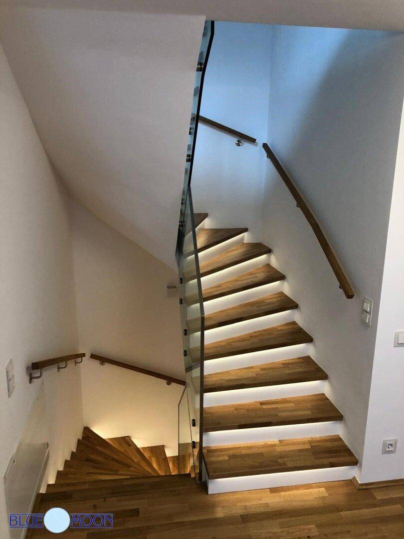 Moderne Holztreppe mit beleuchteten Stufen und Glasgeländer im Flurbereich.